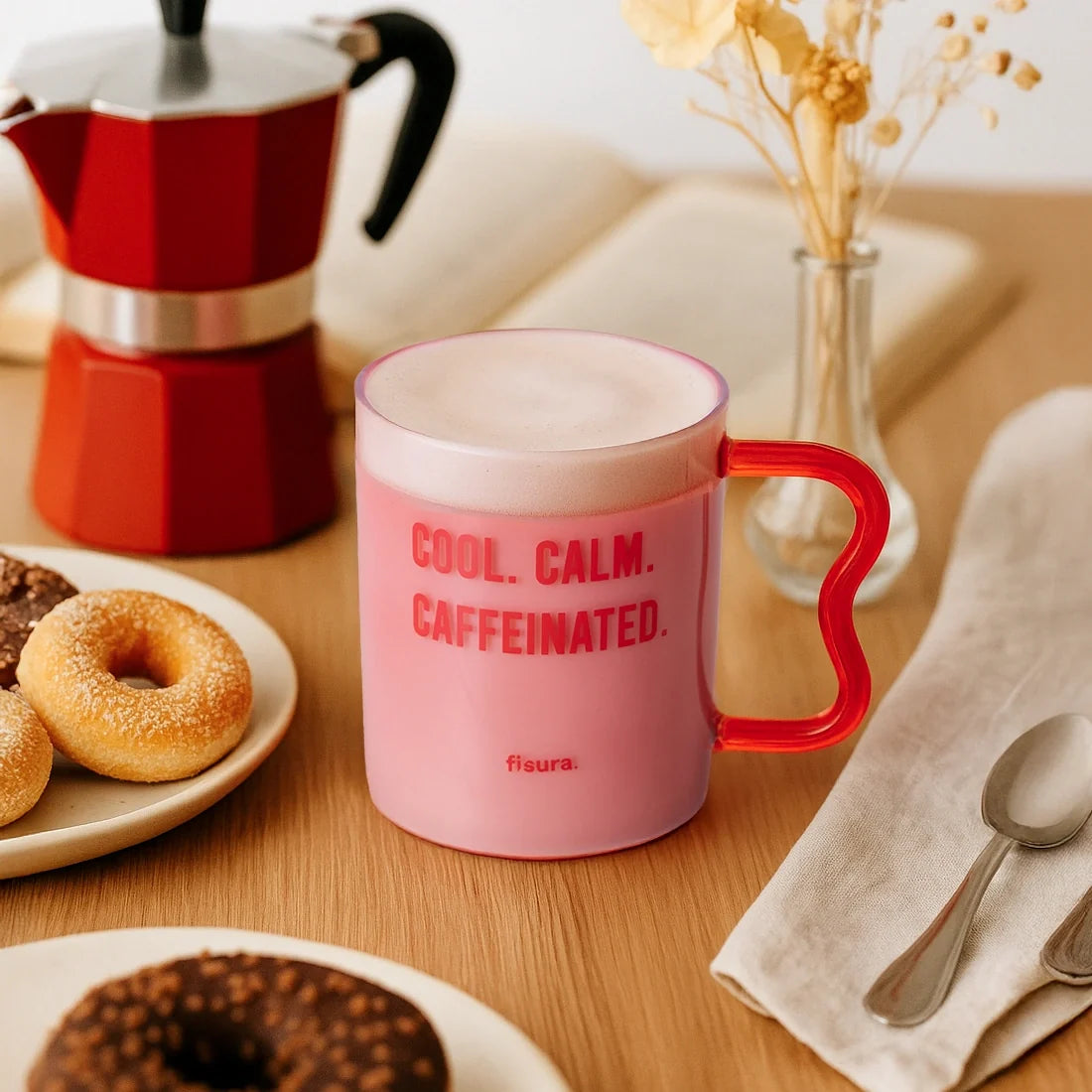 Pink glass mug on a wooden table with doughnuts and a moka pot