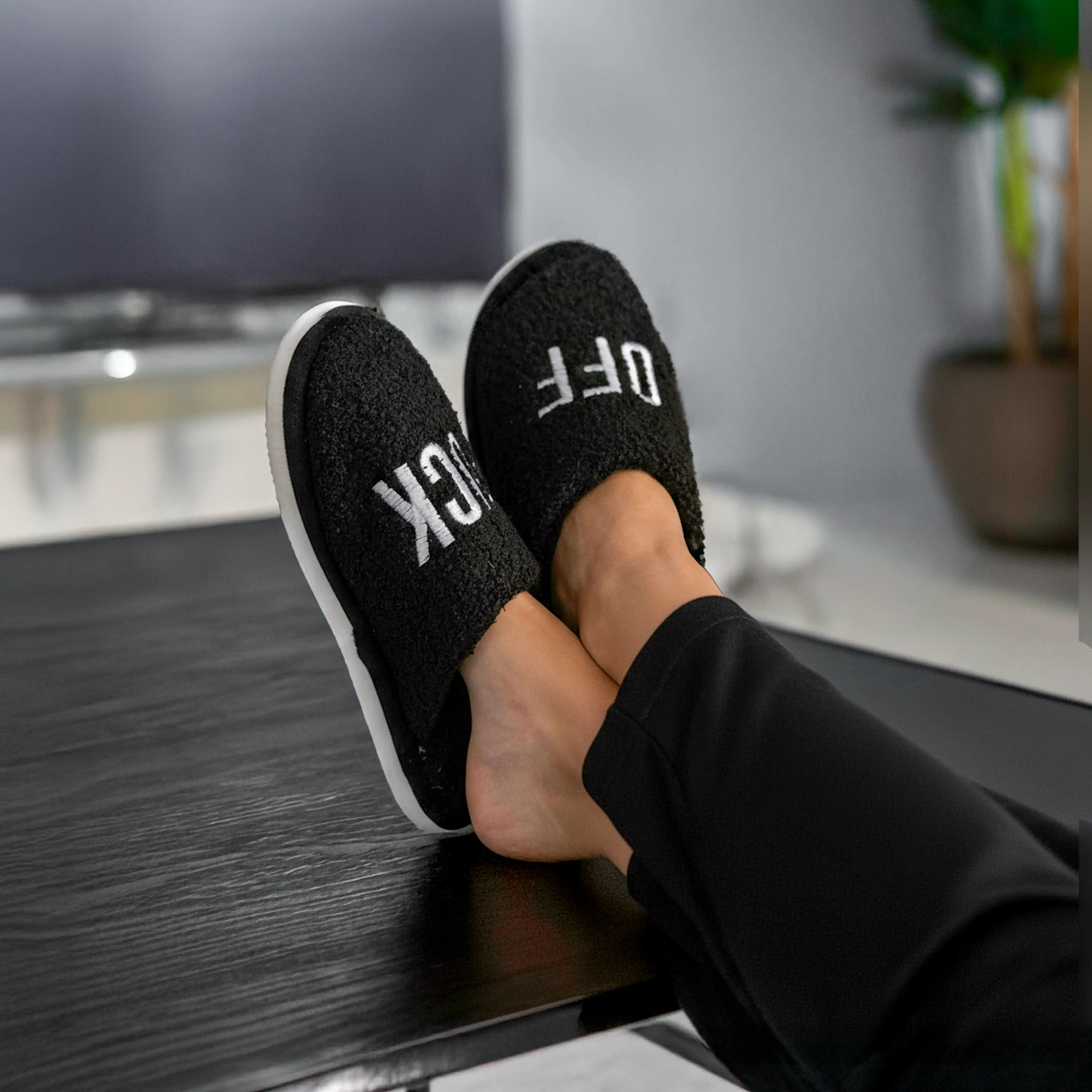 Feet in black slippers resting on a dark wooden floor