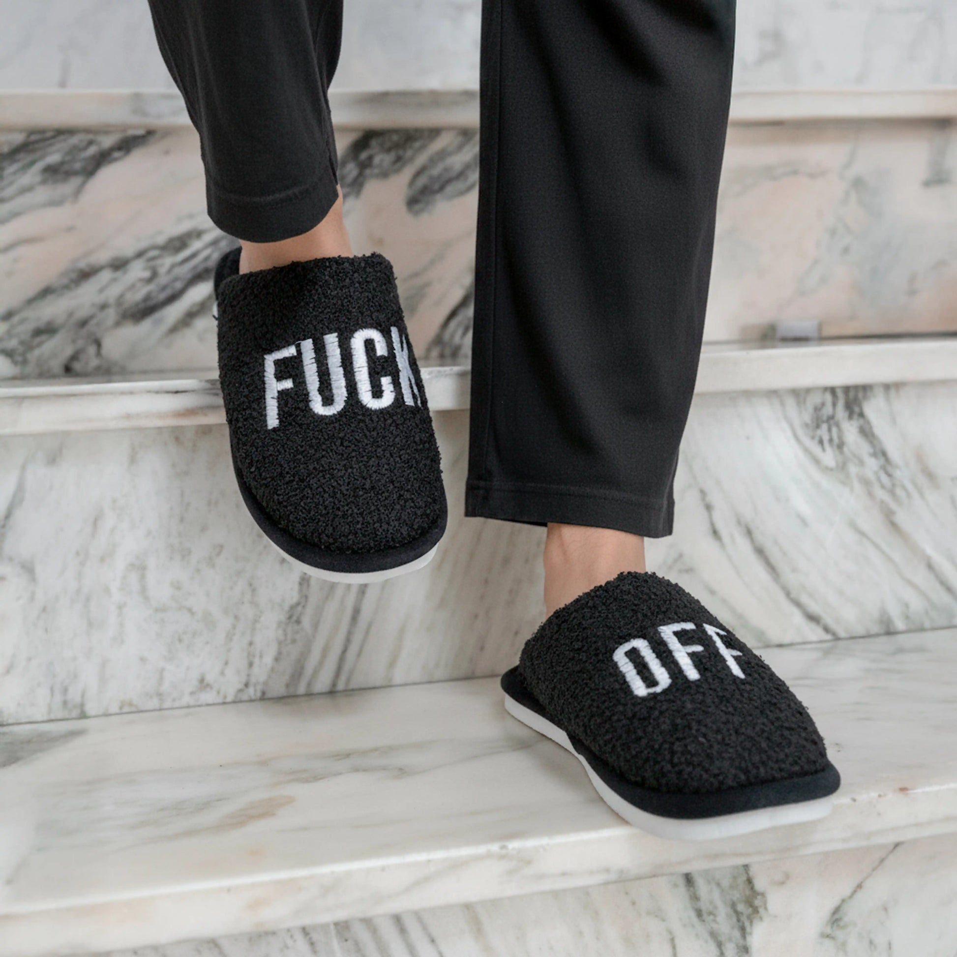Black slippers being worn on a pale marble floor
