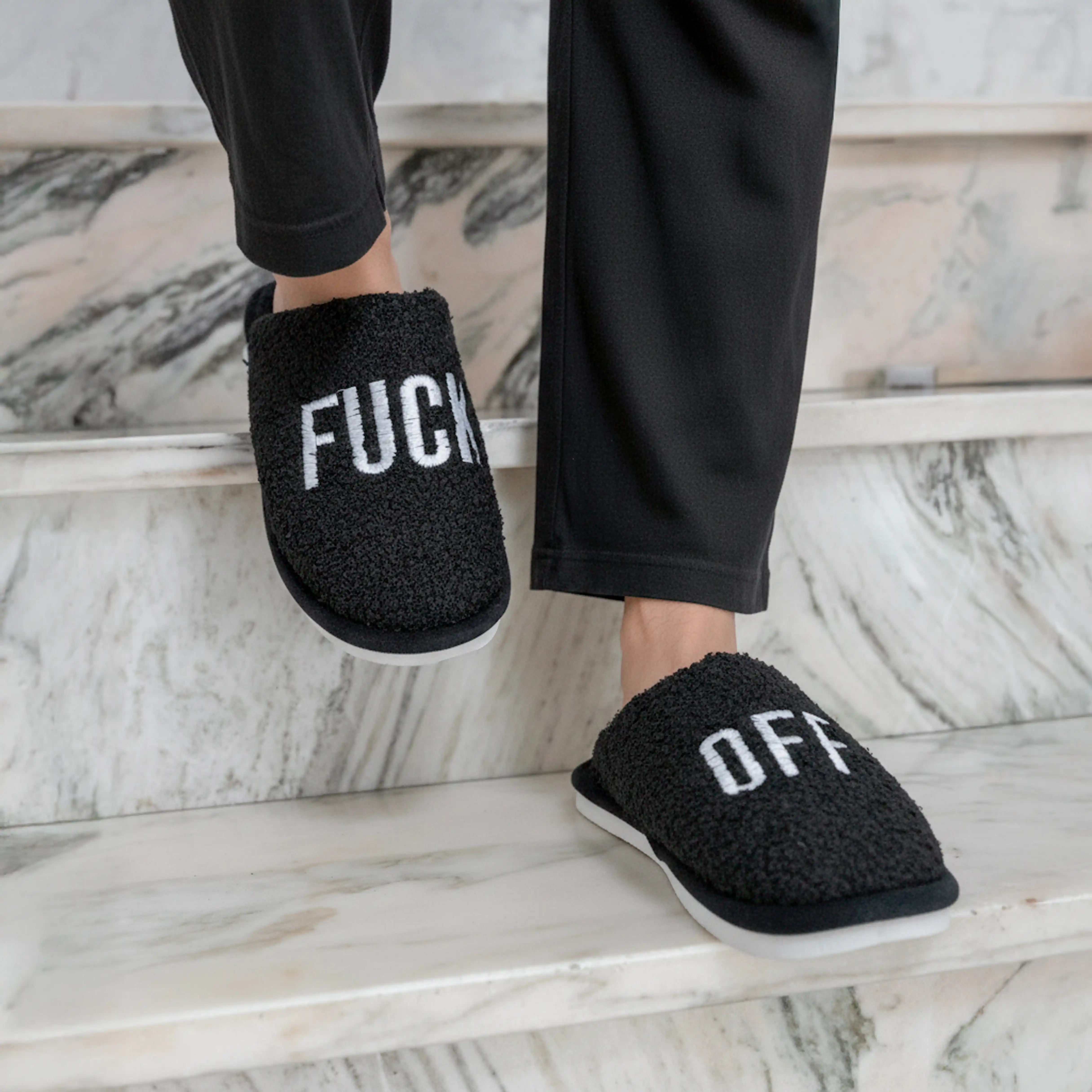 Black slippers being worn on a pale marble floor