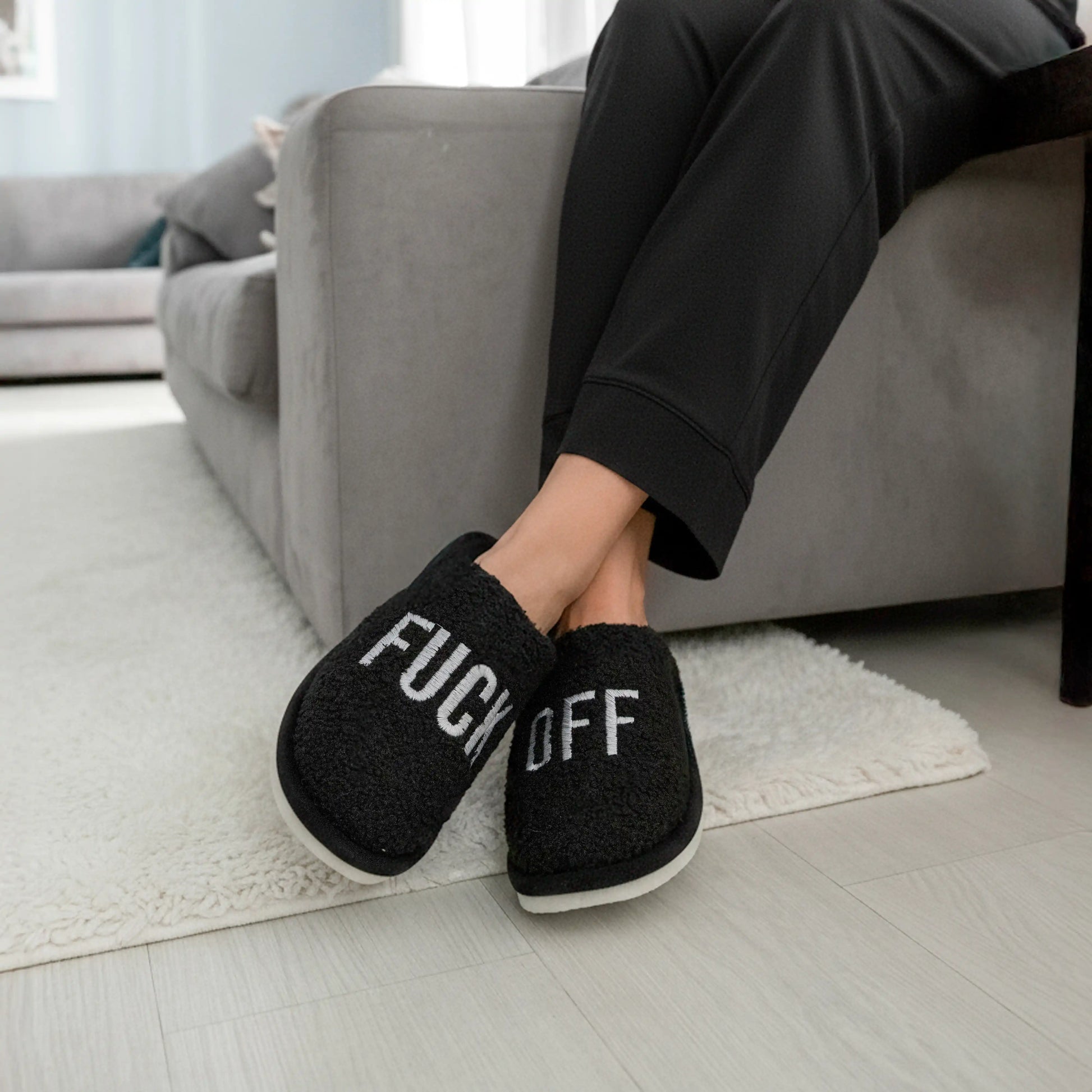 Black slippers on a cream rug beside a light grey sofa