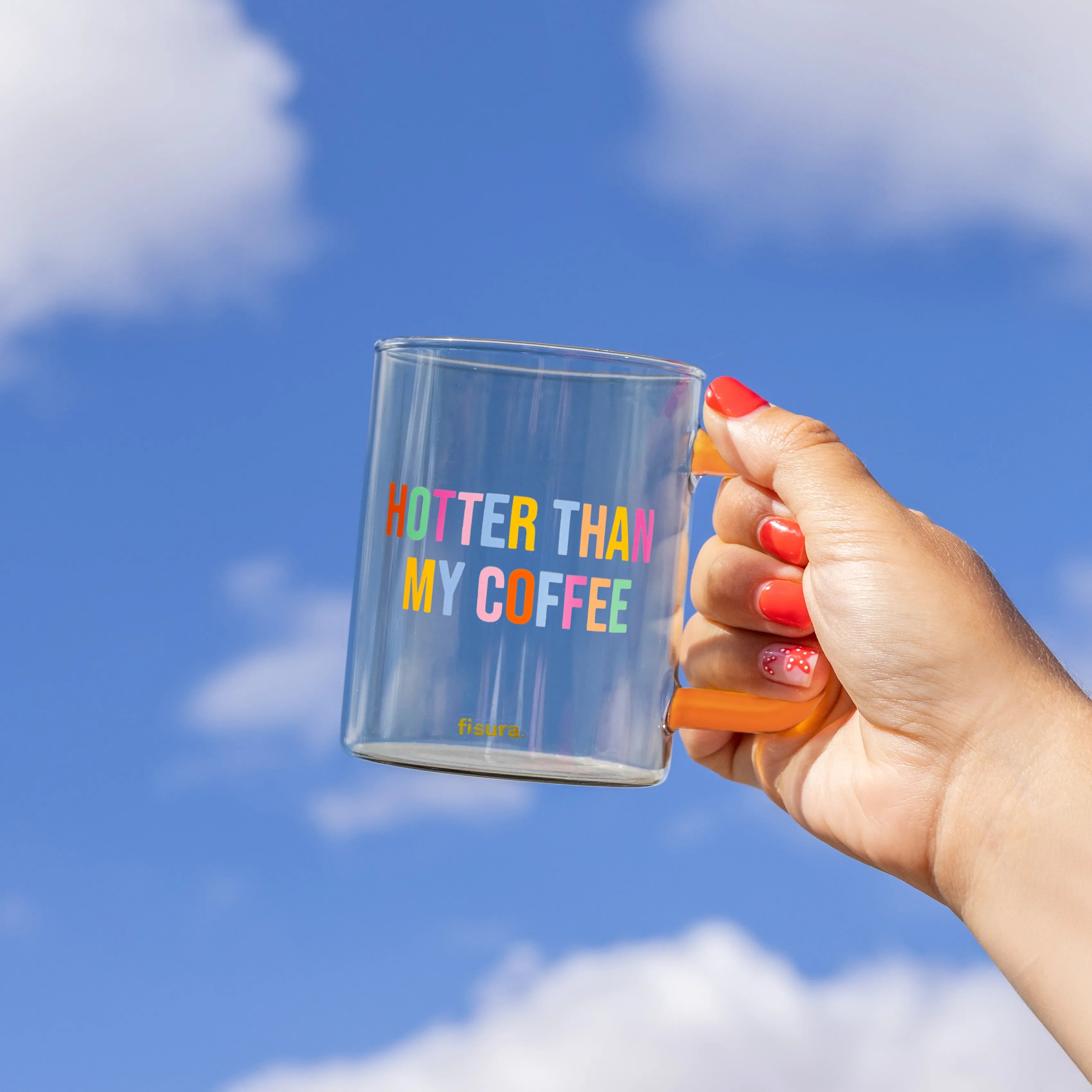 Hand holding the glass mug up against a bright blue sky