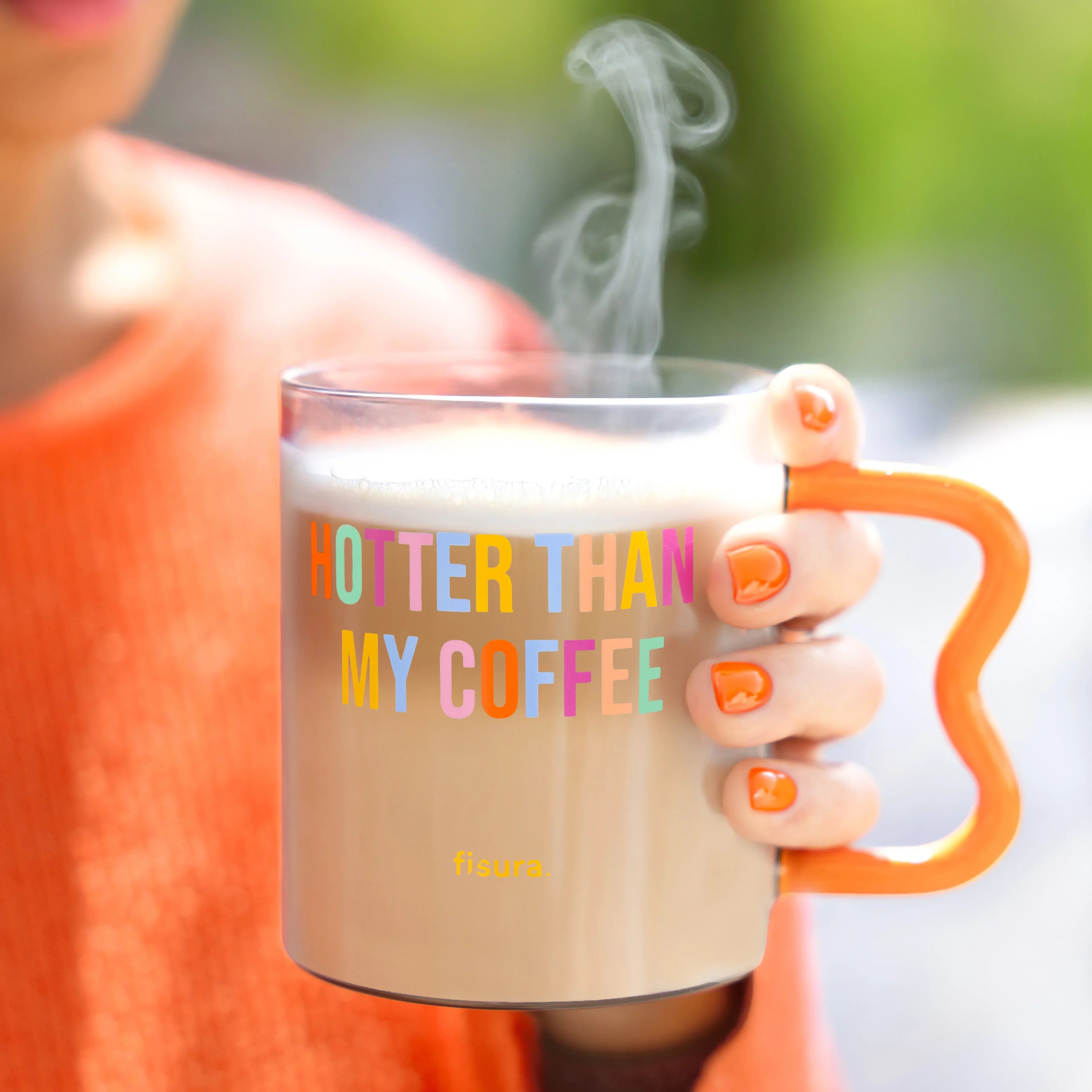 Person in orange holding the steaming glass mug in both hands