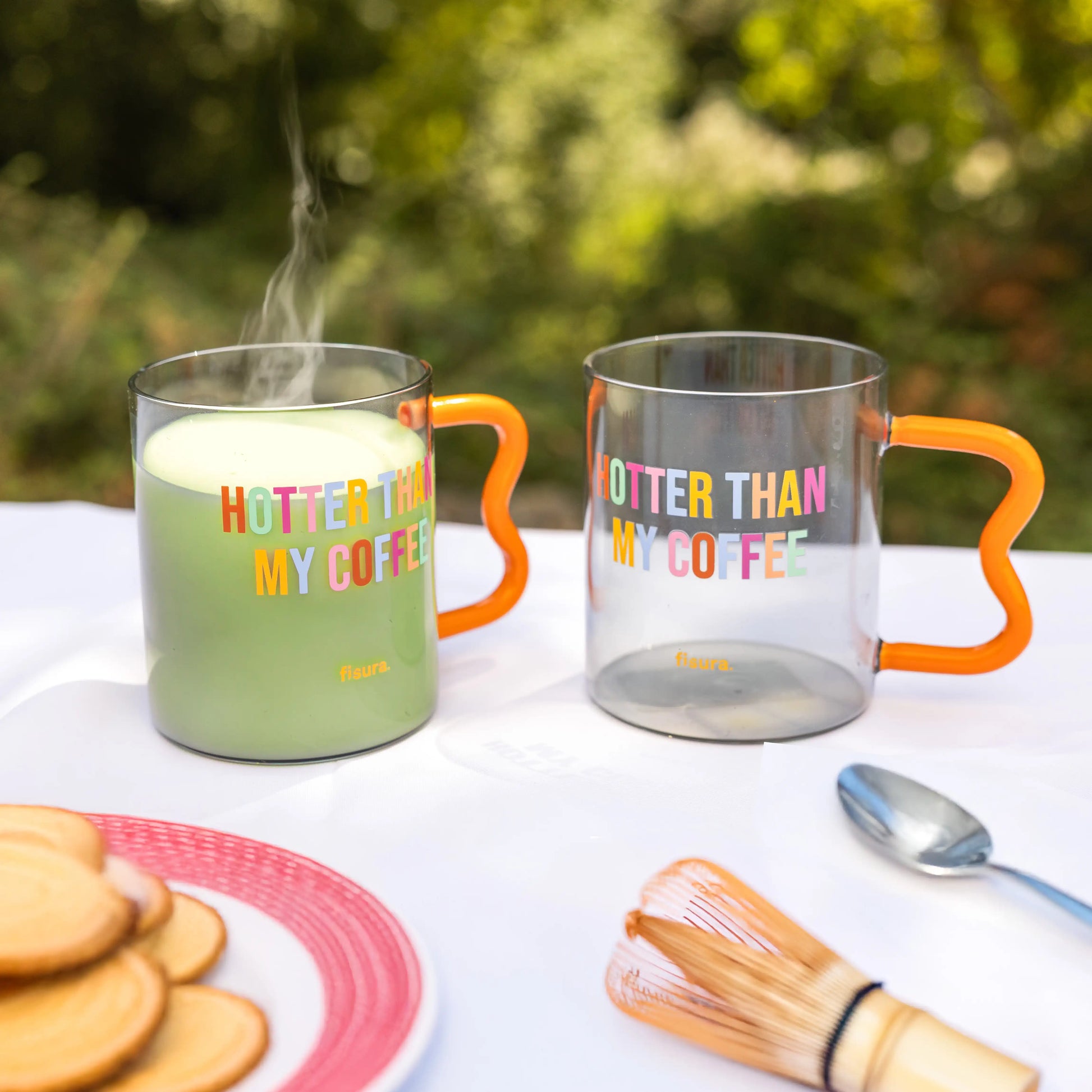 Glass mug of tea on an outdoor table beside a candle and biscuits