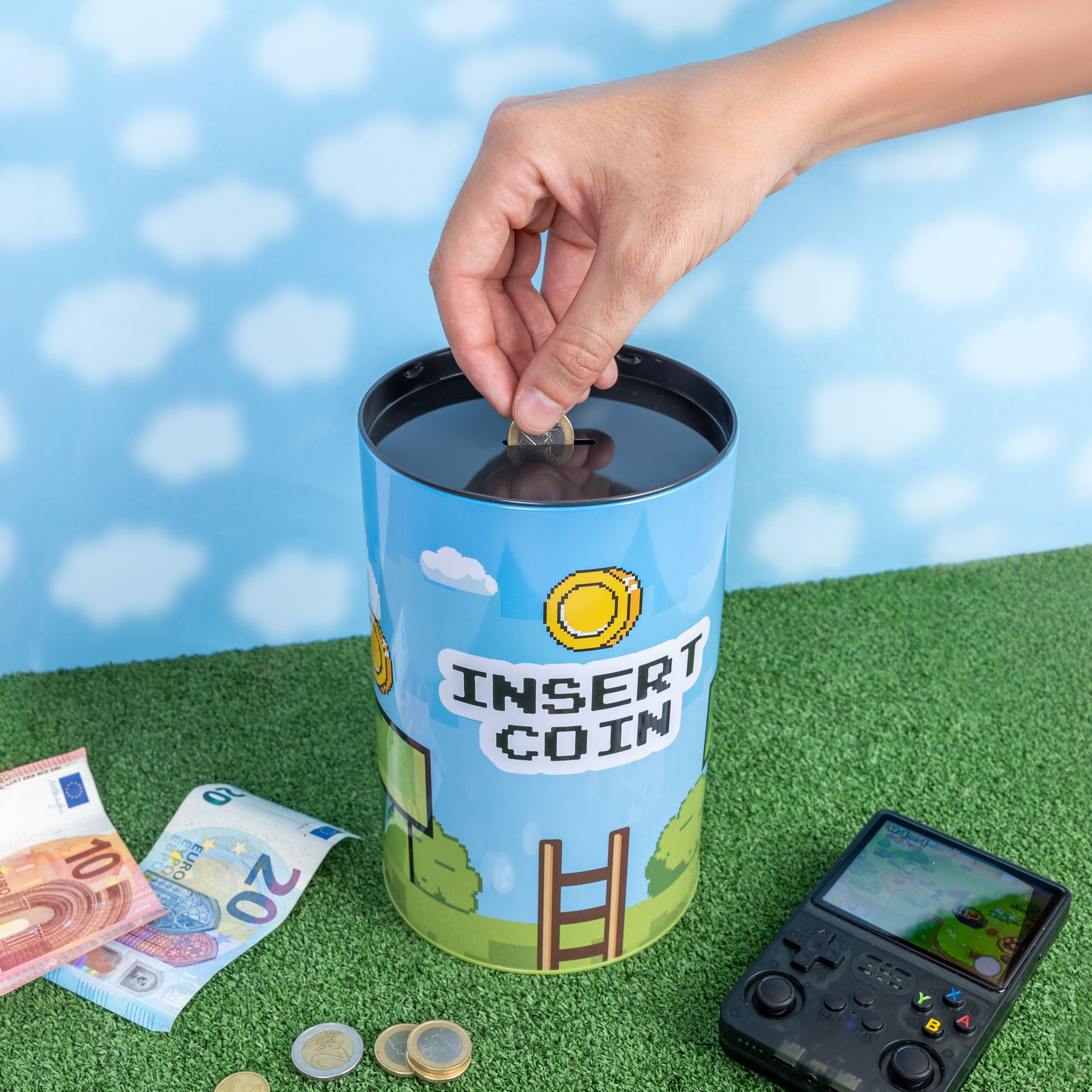 Hand dropping a coin into the Insert Coin tin on green grass