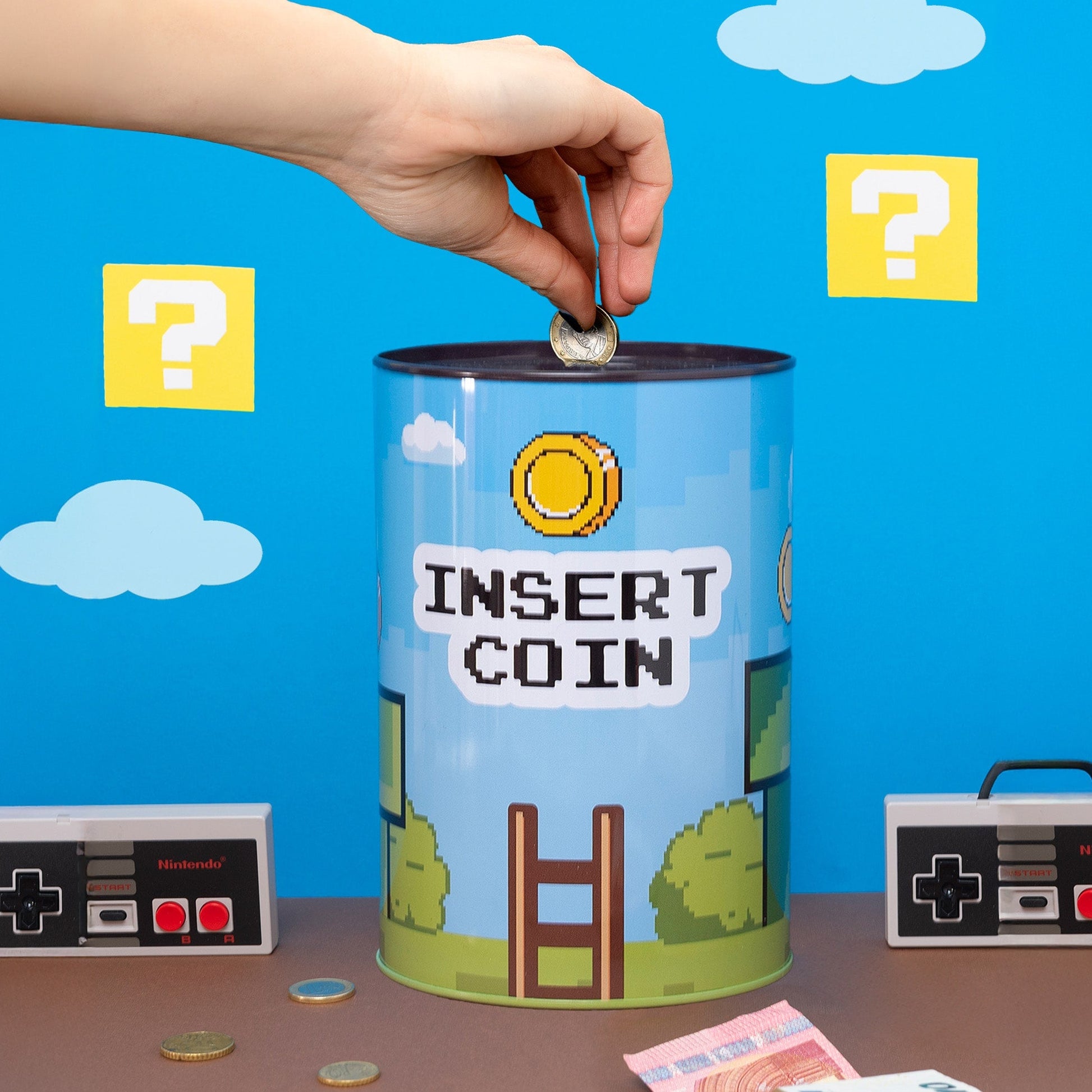 Hand posting a coin into the Insert Coin tin against a pixel sky backdrop