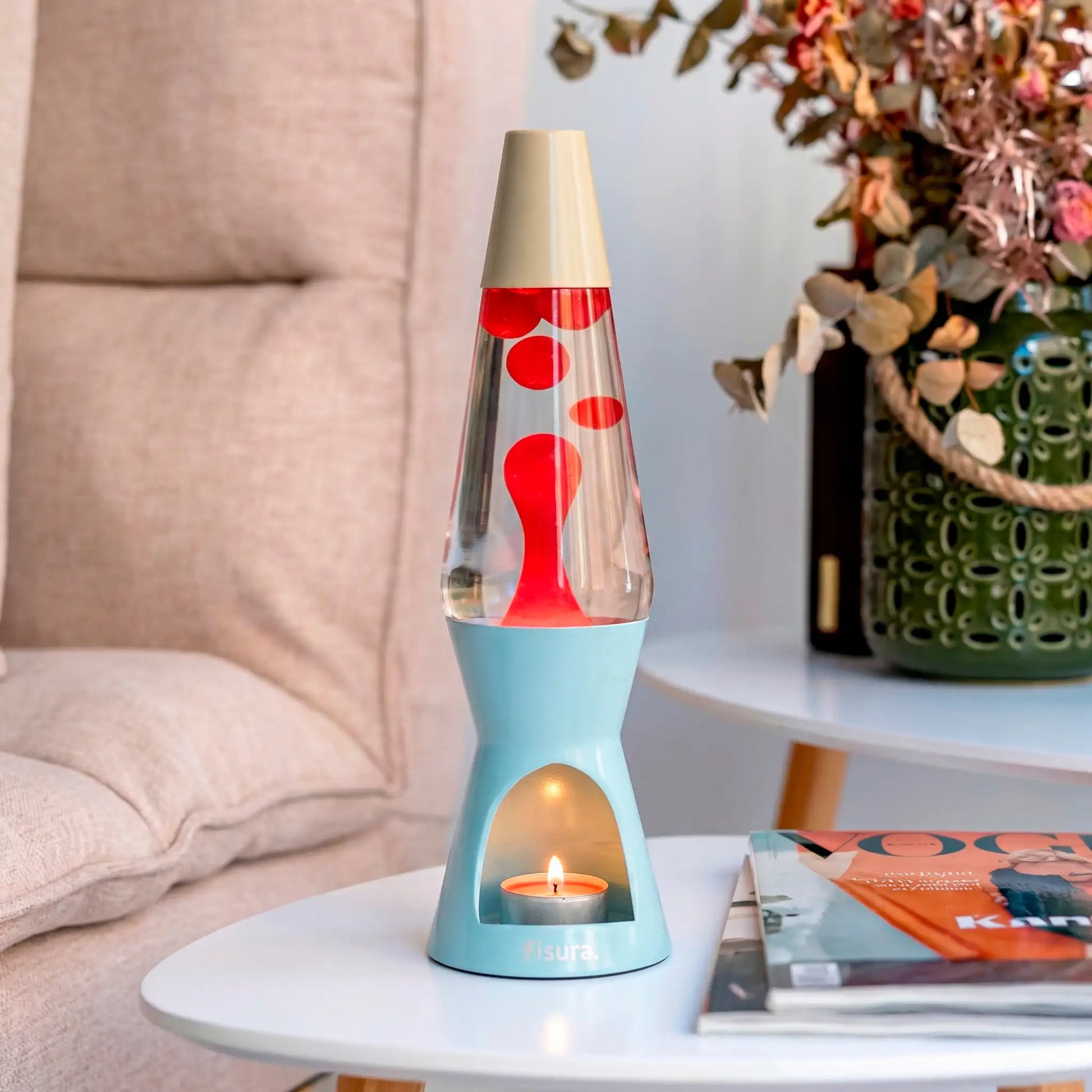 Blue lava candle lamp on a white side table beside dried flowers