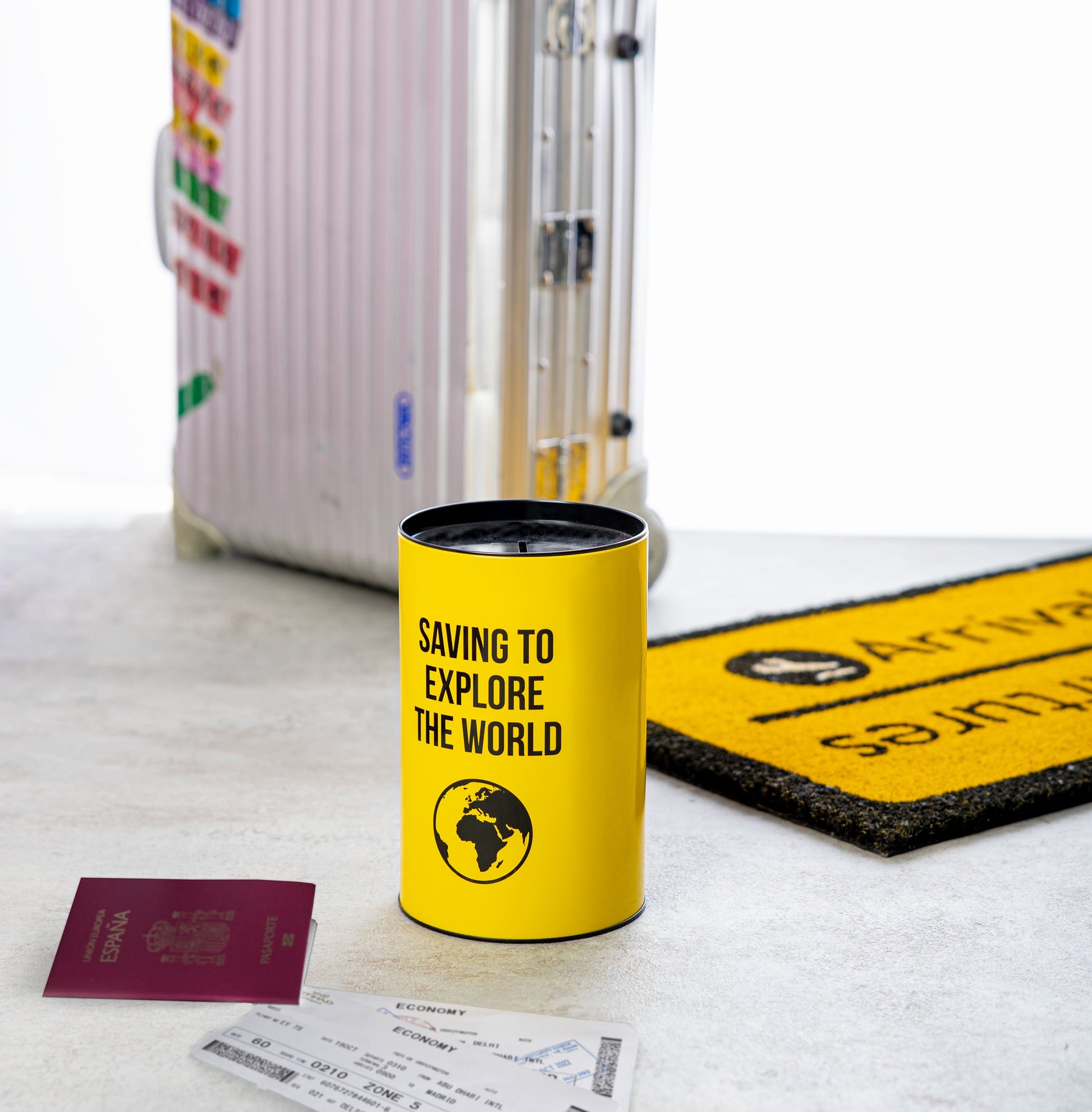 Travel savings tin on the floor beside a suitcase and passport