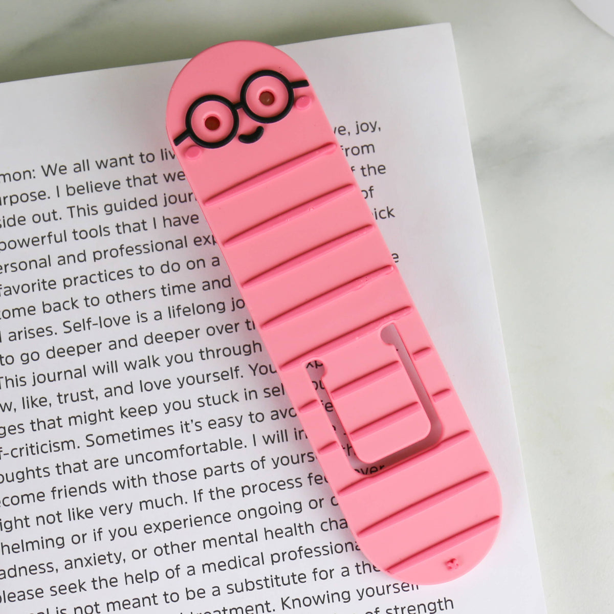 Pink bookworm reading light clipped to an open book