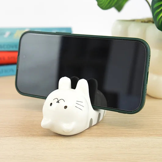 Ceramic cat phone stand holding a smartphone on a wooden desk