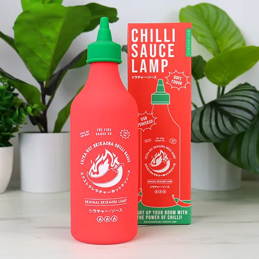 Chilli sauce bottle lamp beside its box with plants behind