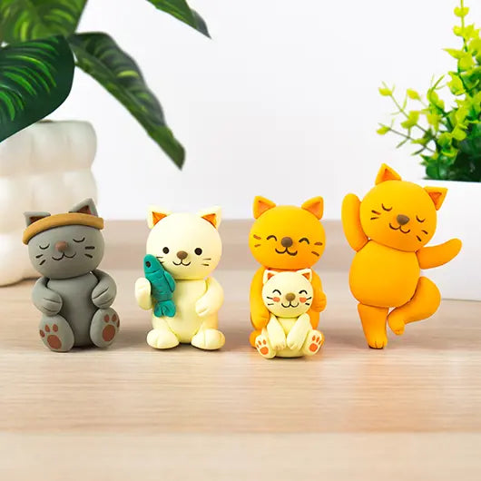 Four finished clay cats sitting in a row on a table with plants