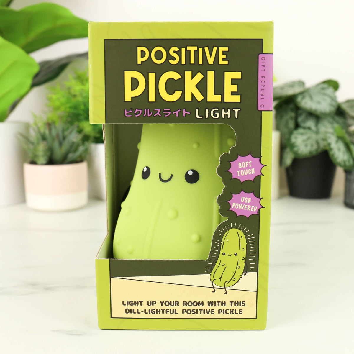 Positive Pickle Light beside its box on a white shelf with plants