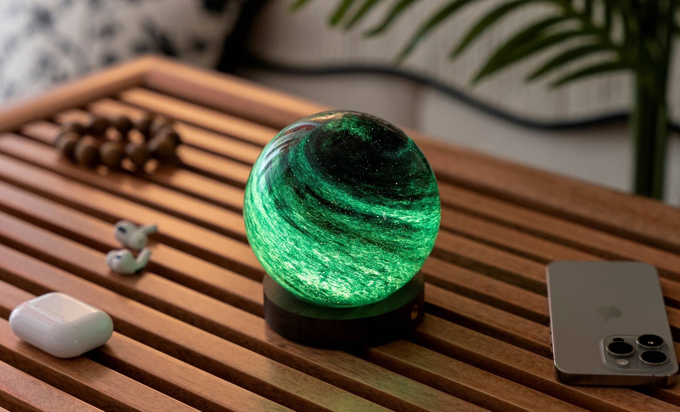 AstraGlass light glowing emerald green on coffee table with AirPods