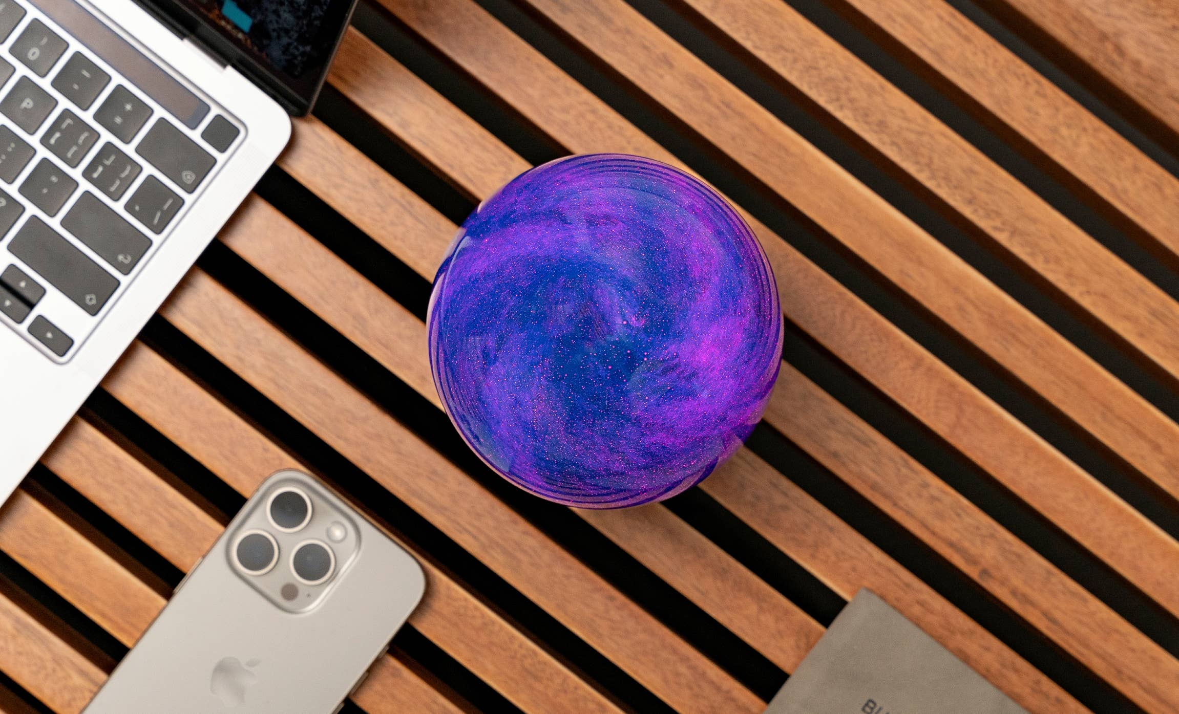 AstraGlass Galaxy Breeze orb from above glowing violet beside laptop