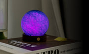 AstraGlass mini light glowing purple and blue on walnut base on books