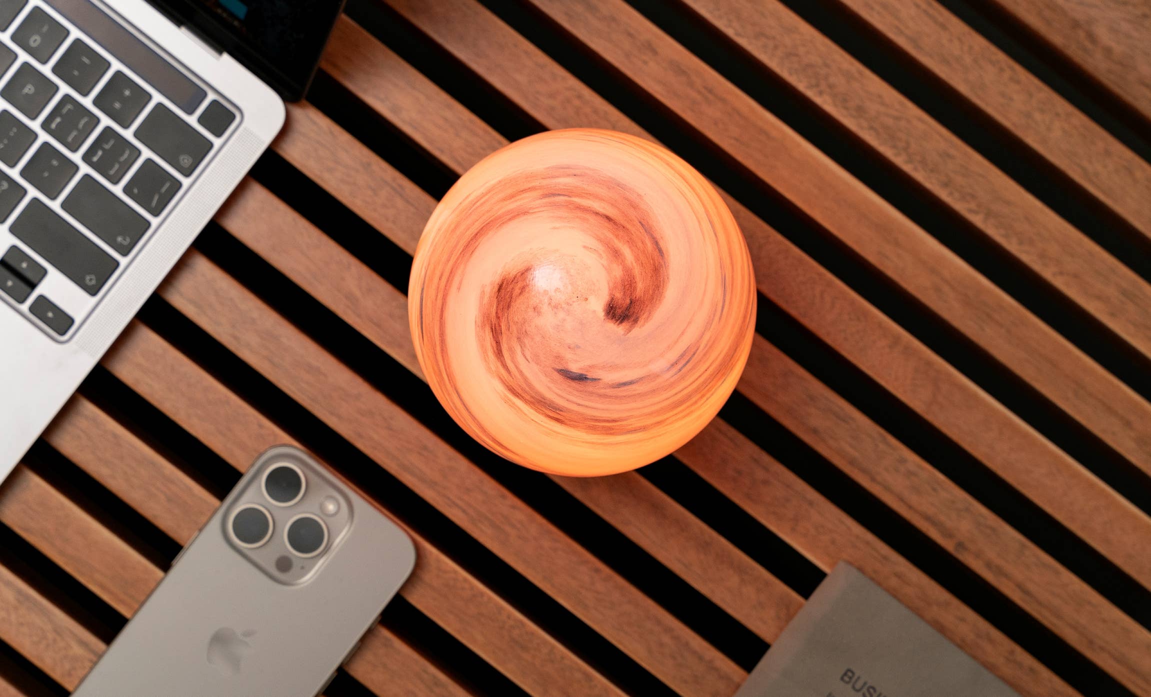 AstraGlass orb from above glowing soft orange swirl beside laptop