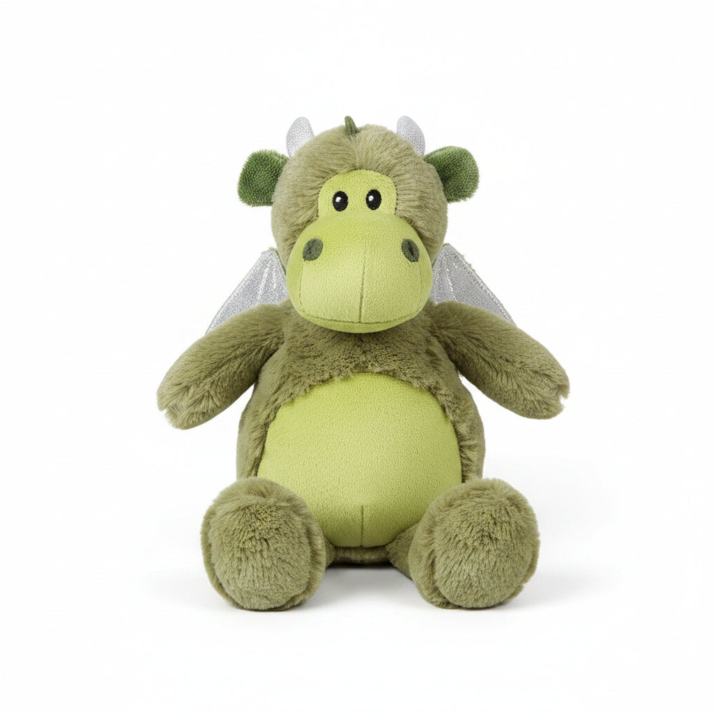 A plush toy dragon in olive green and light yellow-green, sitting on a white wooden plank surface. The dragon has silver glittery wings, small white horns, and embroidered facial features.