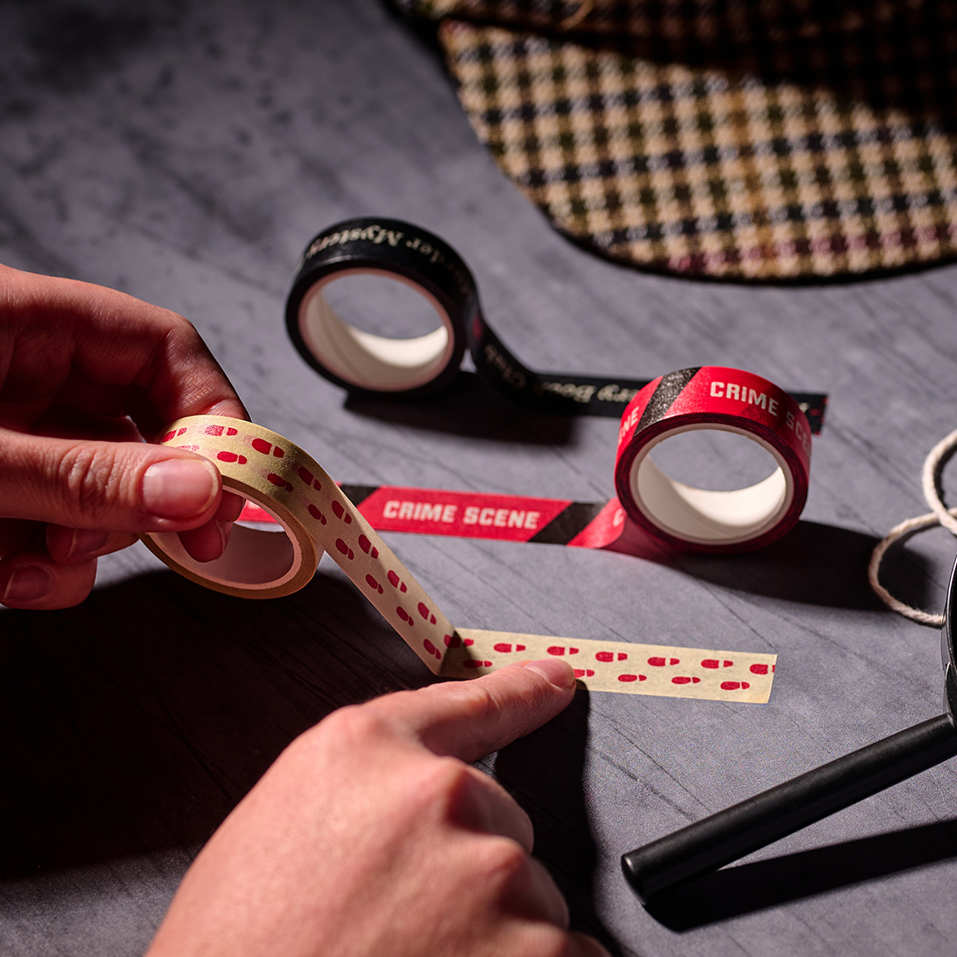 Hand tearing a strip of crime scene washi tape at a desk with scissors