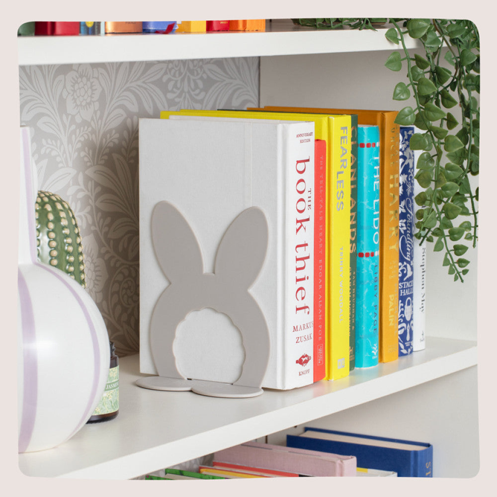Stone bunny bookends holding books upright on a white shelf