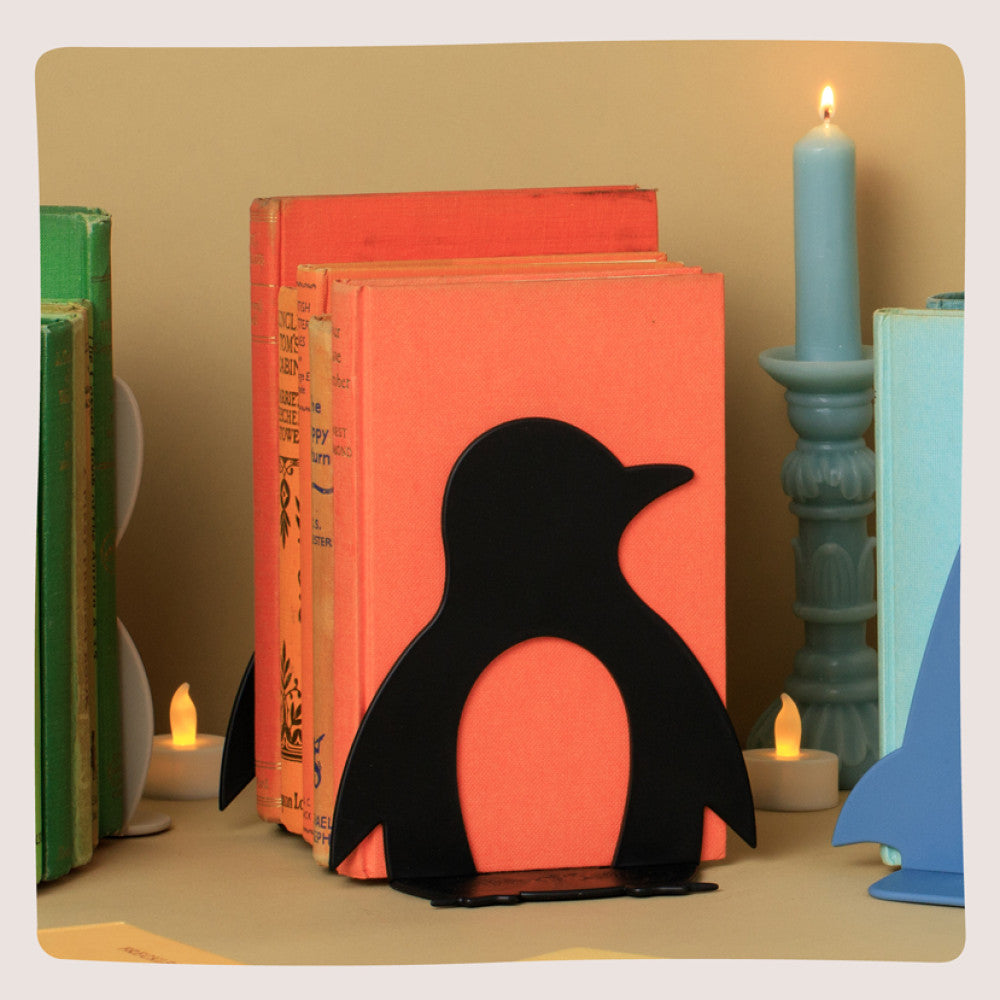 Black penguin bookend propping up orange books beside lit candles