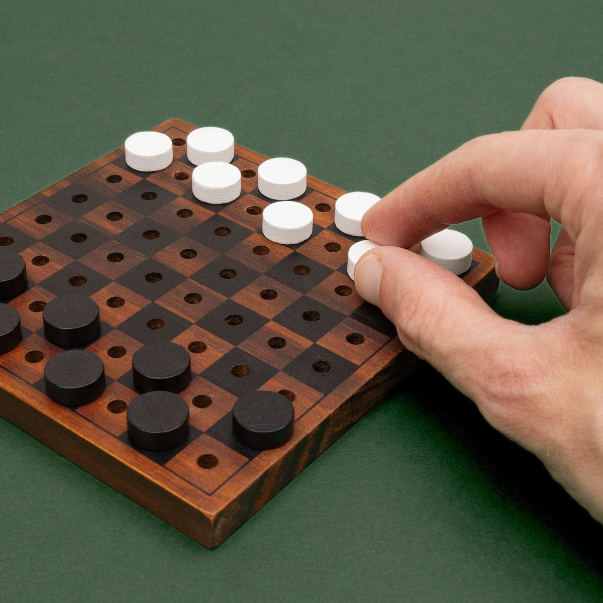 Hand placing white checkers on the Checkmate wooden board, green background