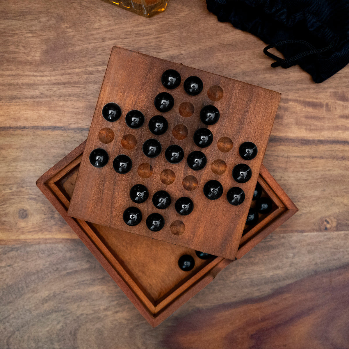 Wooden solitaire game with black marbles on a rich wood table