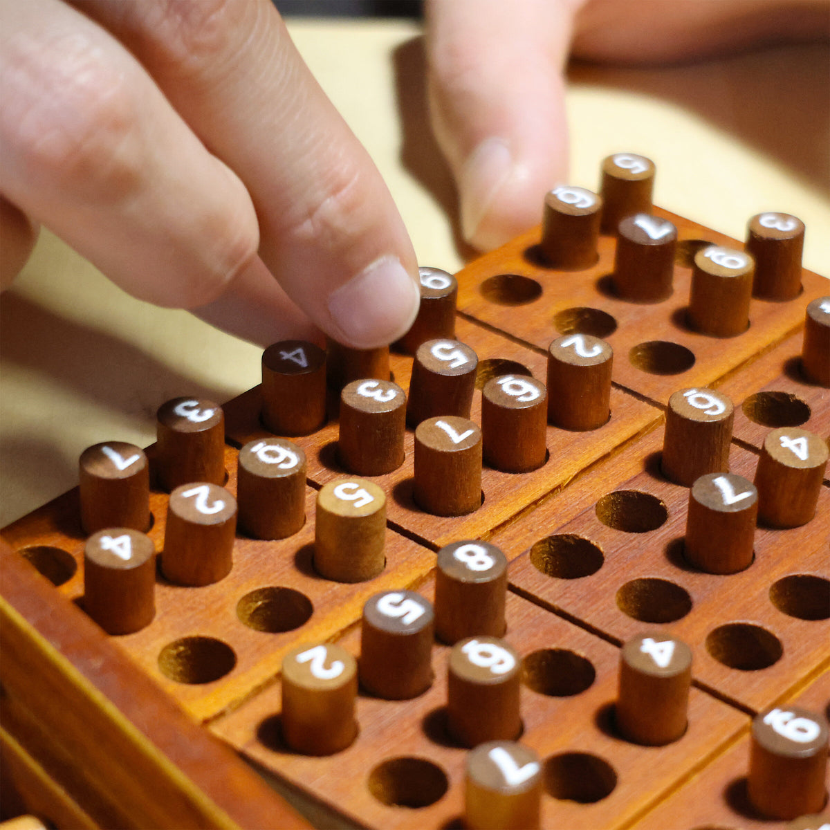 Close up of fingers placing numbered wooden pegs into the sudoku board