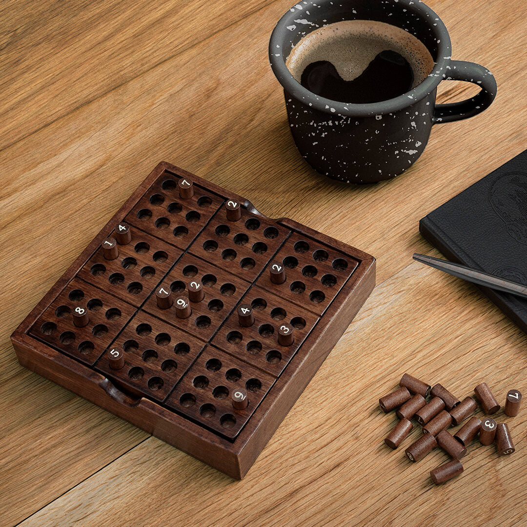 Wooden sudoku puzzle on an oak table beside a coffee cup and notebook