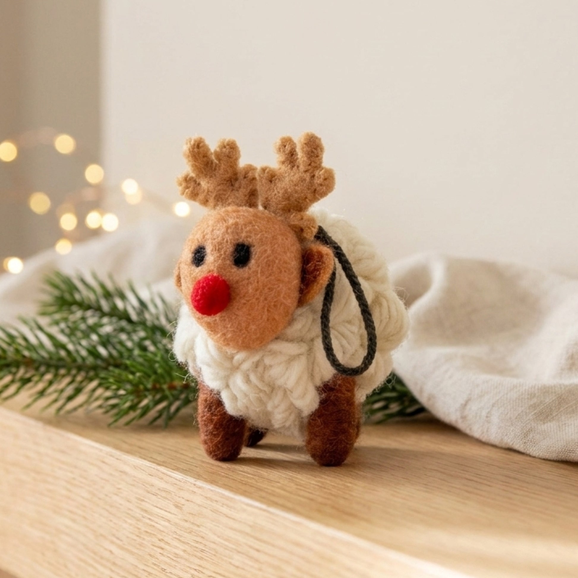 Wool reindeer sheep standing on a wooden mantelpiece with pine and fairy lights