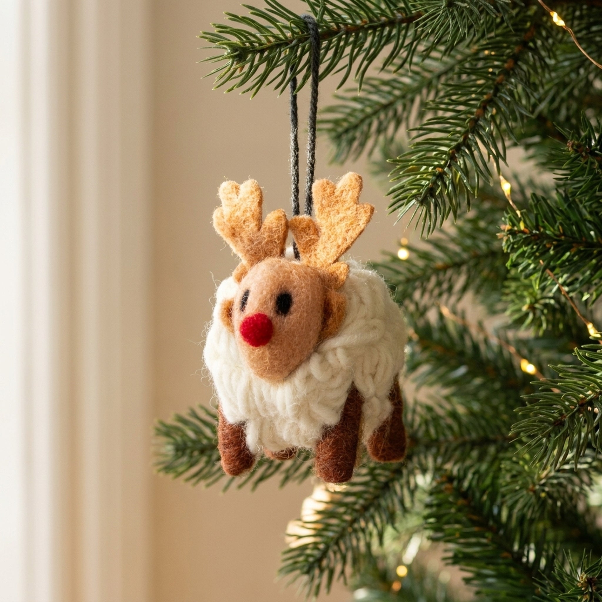 Mini wool reindeer sheep hanging from an evergreen Christmas tree branch