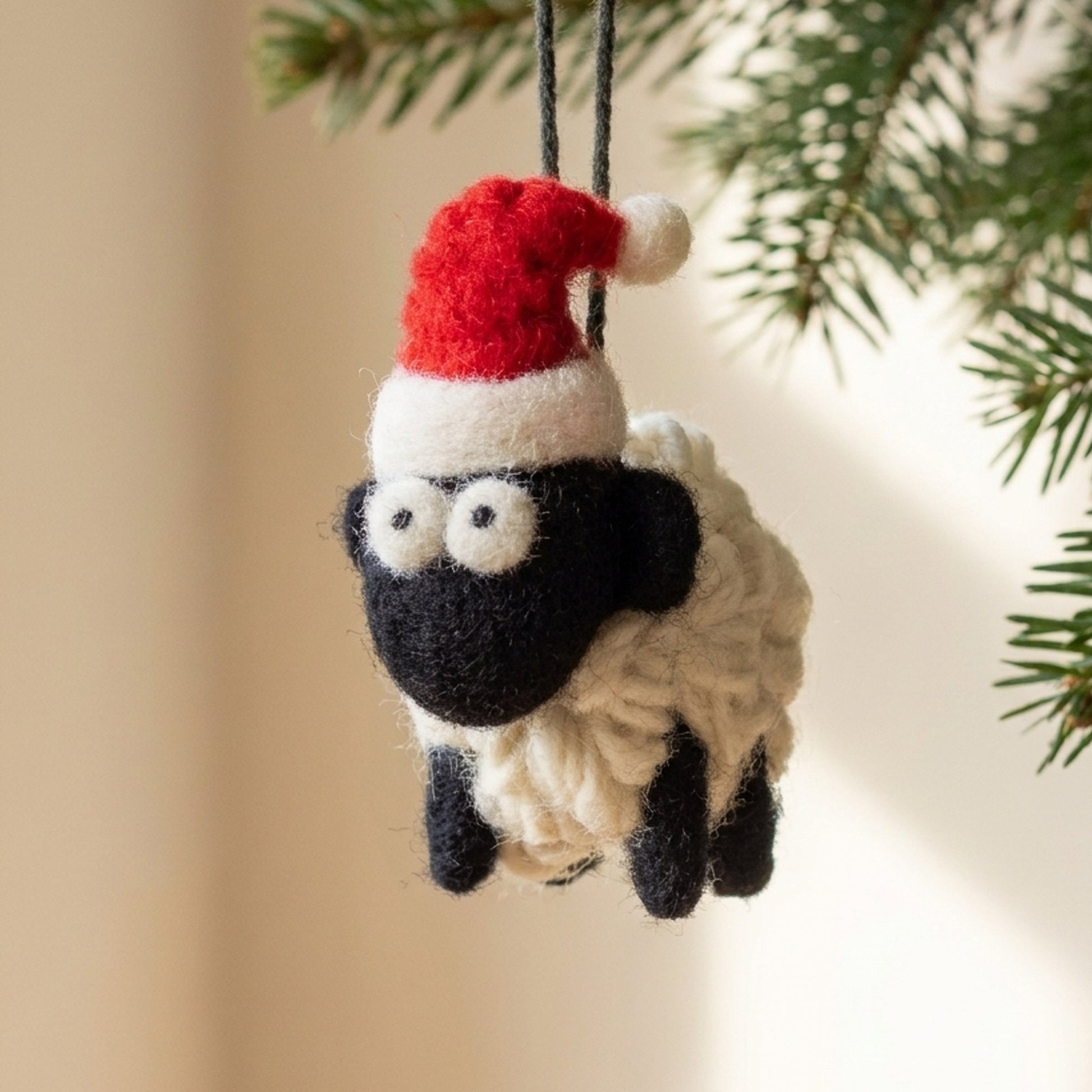 Mini wool Santa sheep hanging from an evergreen Christmas tree branch