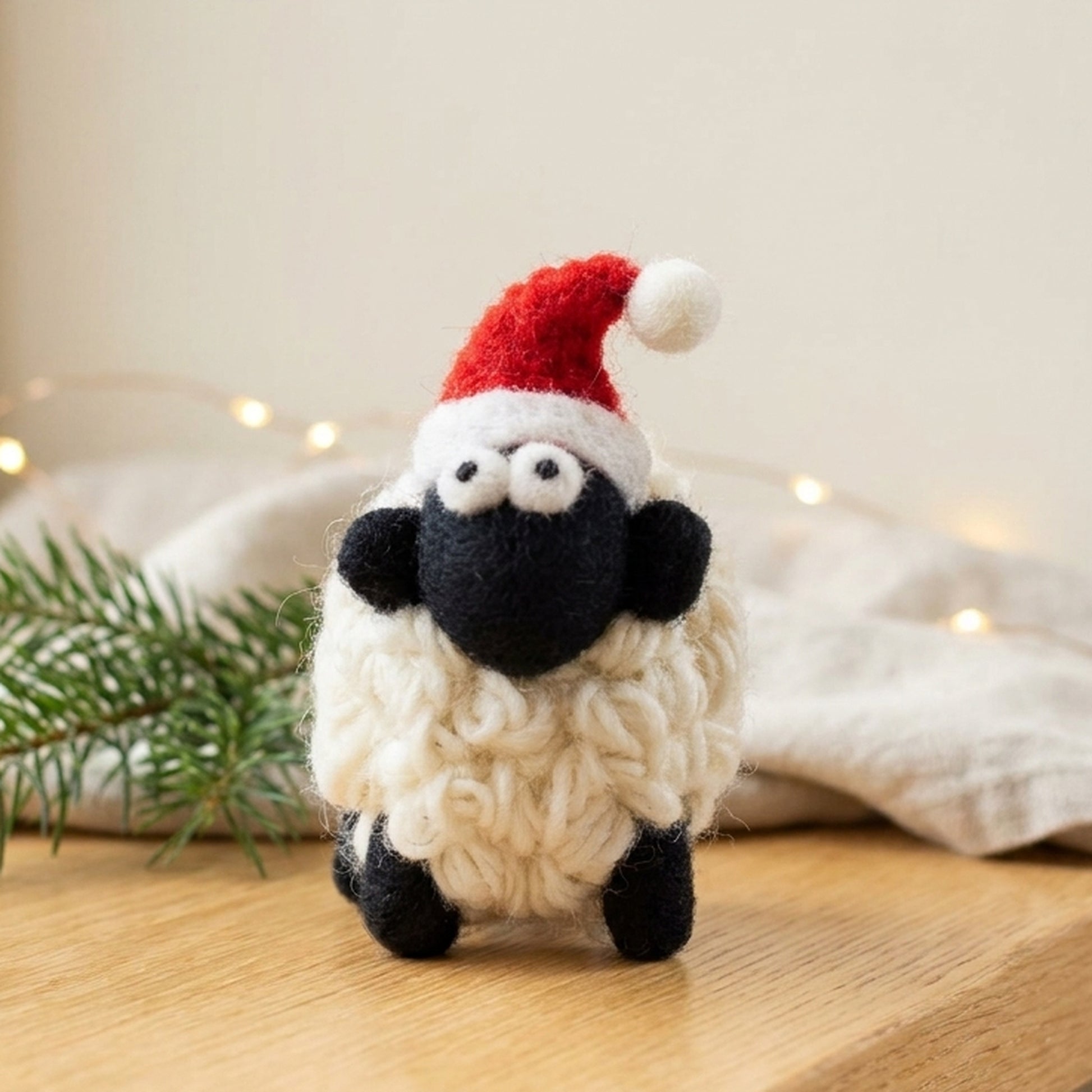 Small wool Santa sheep on a wooden sill with pine and fairy lights behind