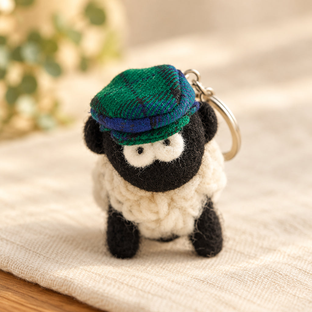 Knitted sheep keyring in blue and green tartan flatcap, second view on white