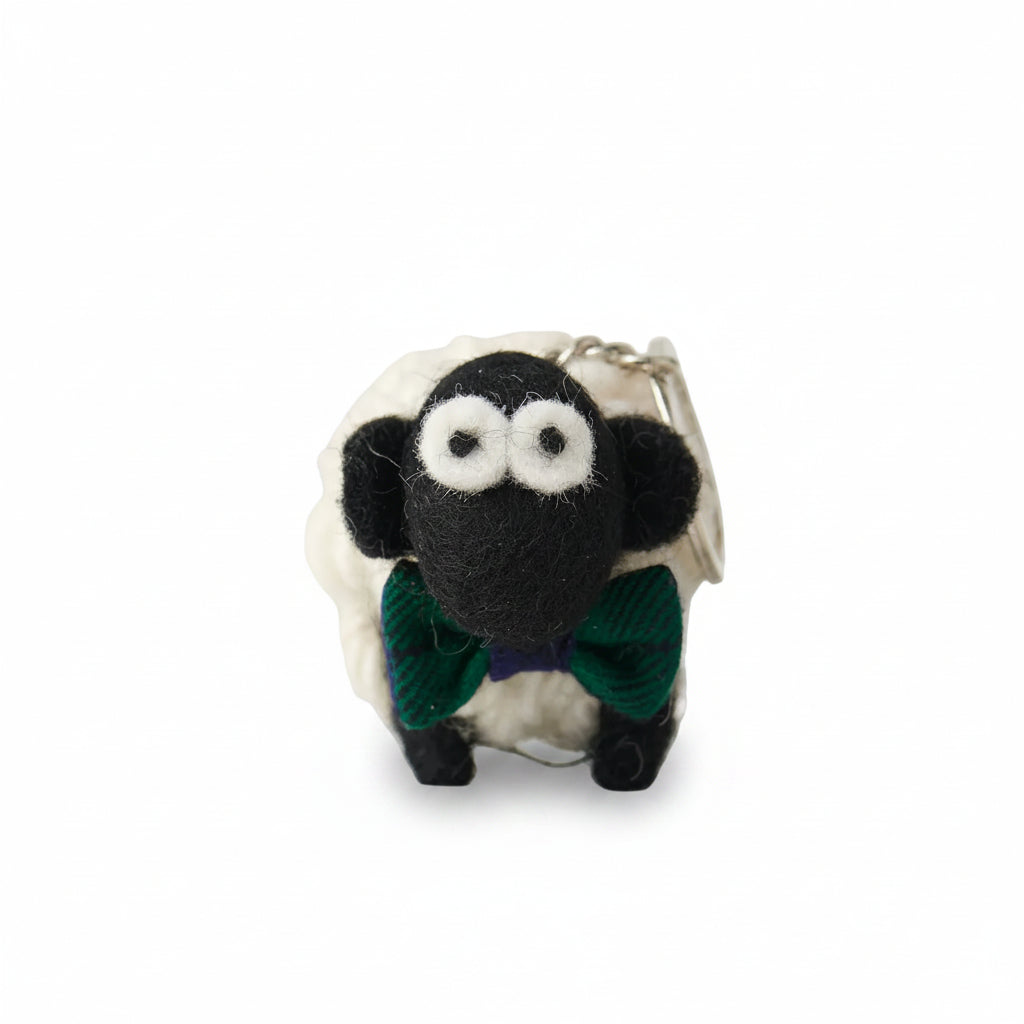 Knitted wool sheep keyring wearing a green tartan bowtie, on a plain grey background.