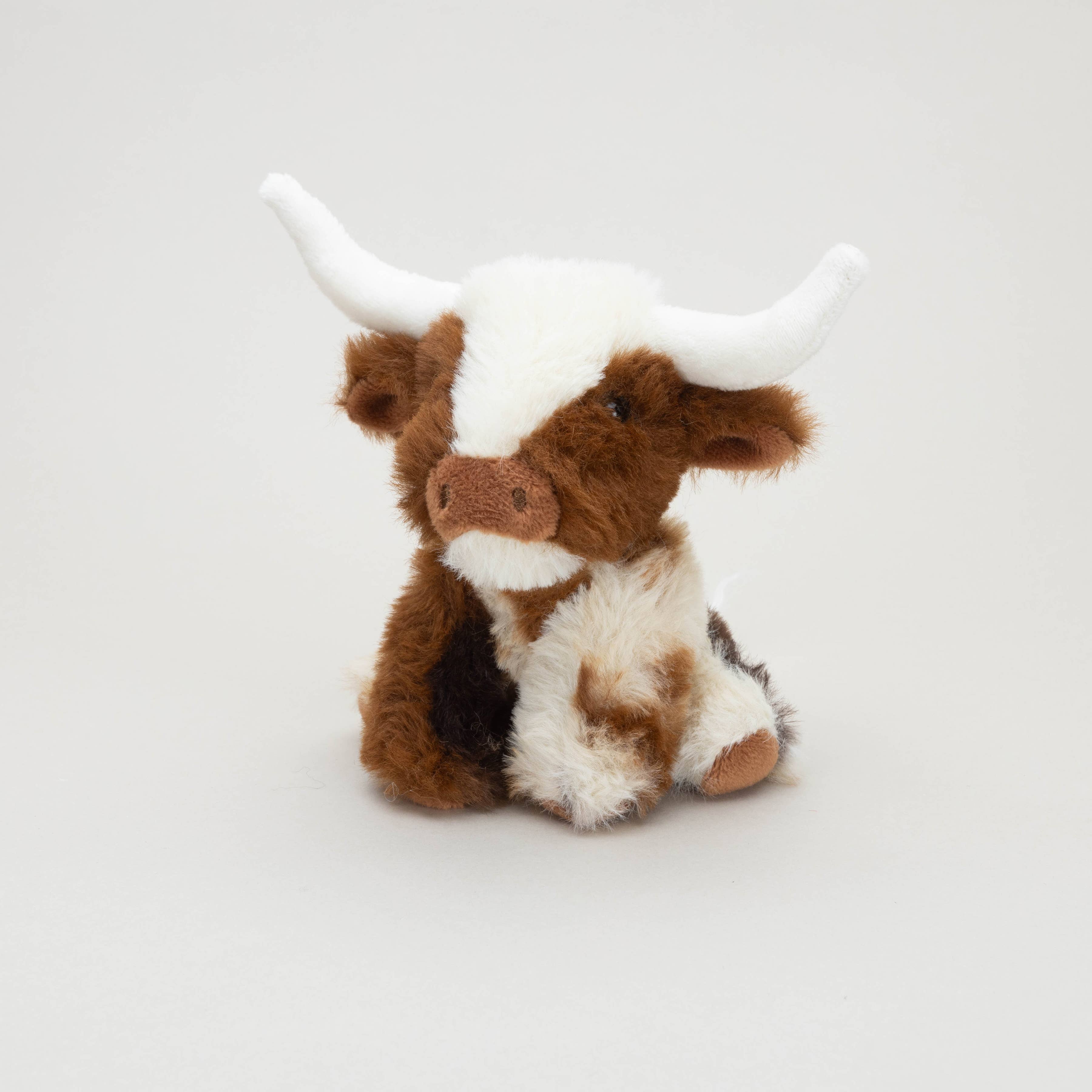 Texas Longhorn mini soft toy cow sitting with white horns on grey background
