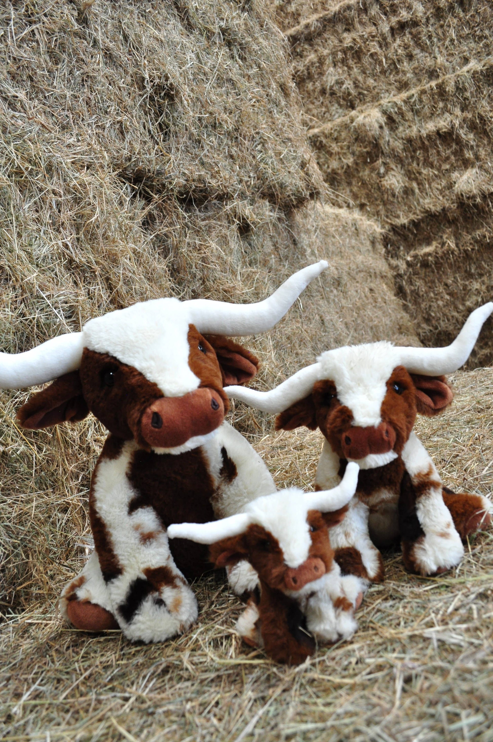 Texas Longhorn soft toy cows in three sizes posed on hay bales