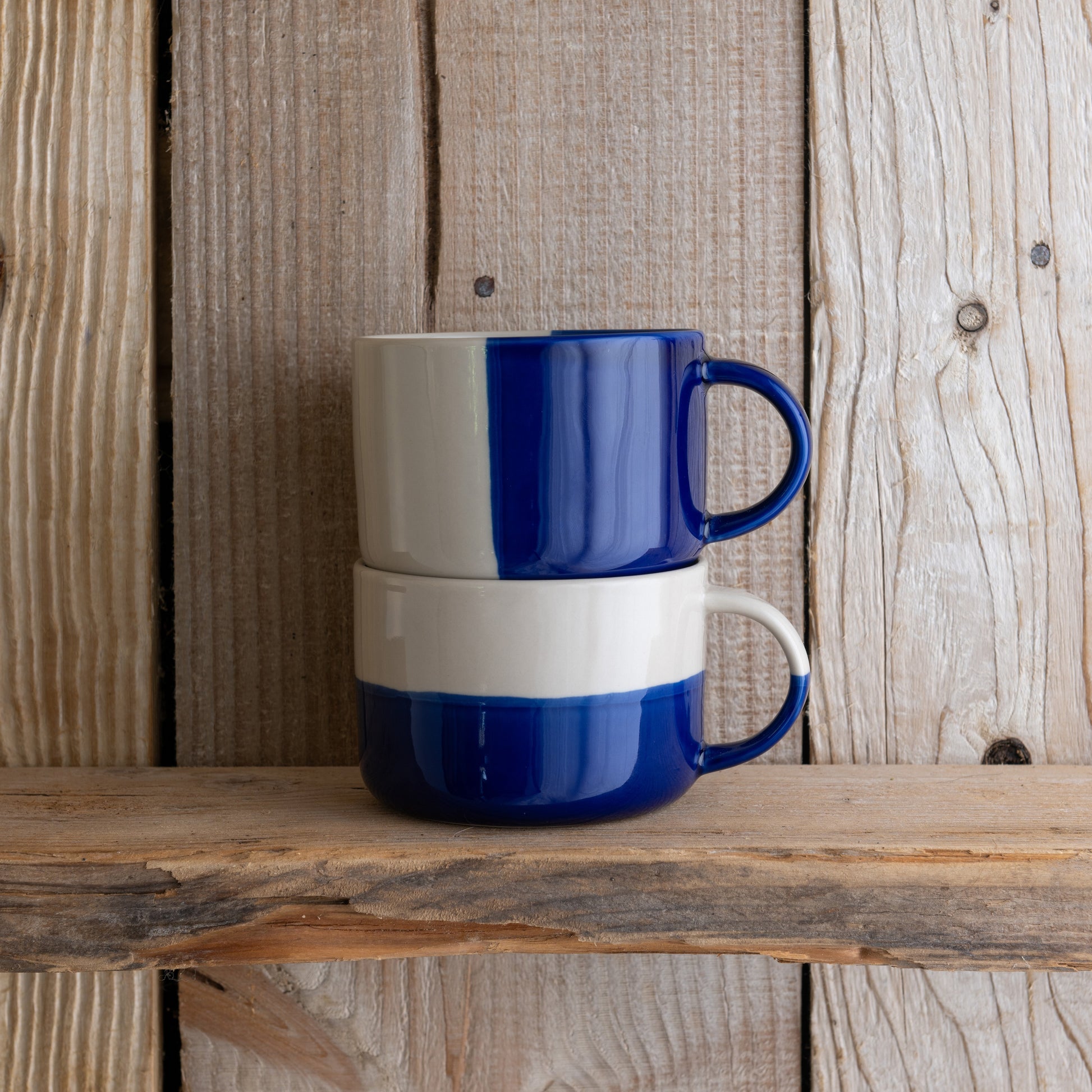 Indigo blue Rue mugs stacked on a weathered wooden shelf