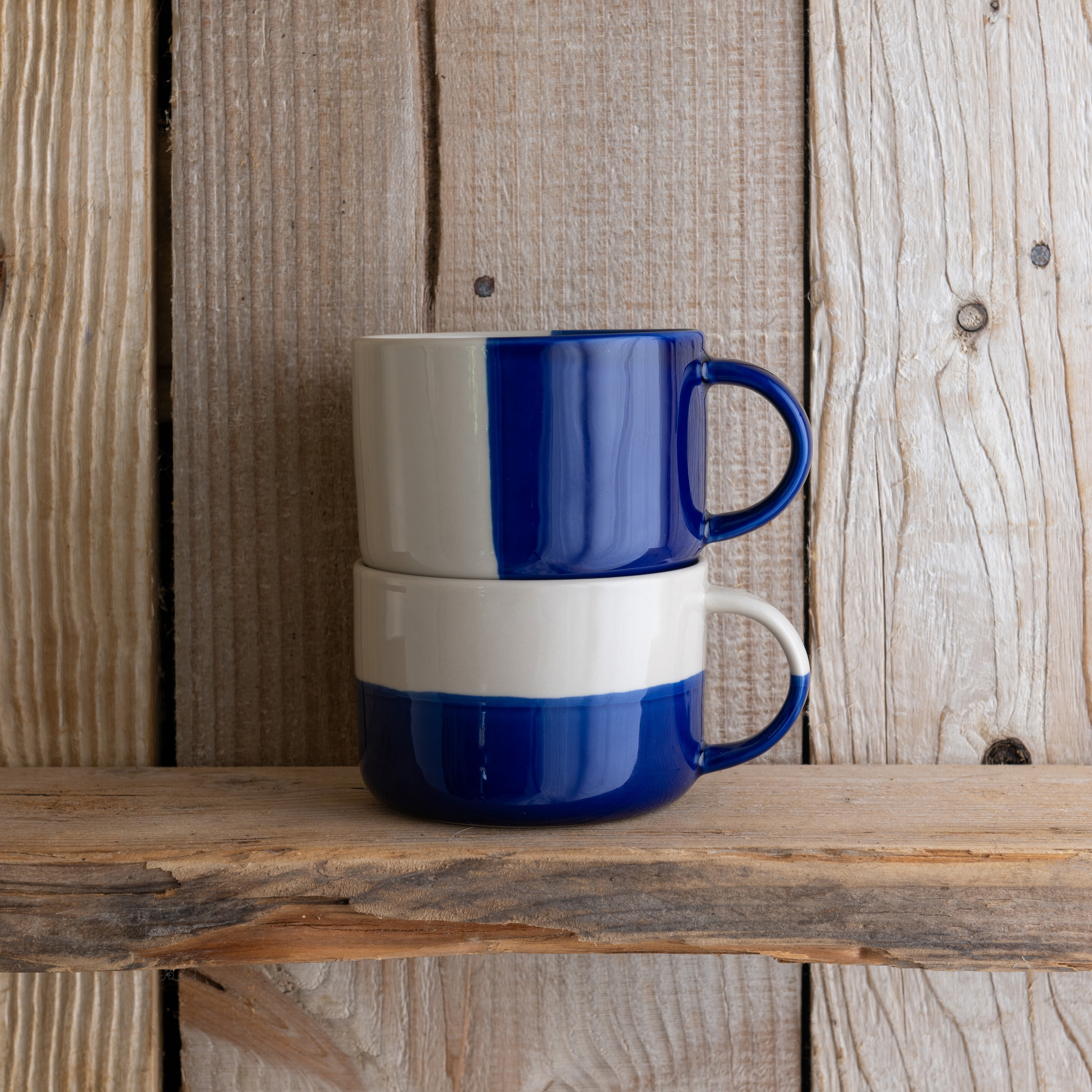 Indigo blue Rue mugs stacked on a weathered wooden shelf