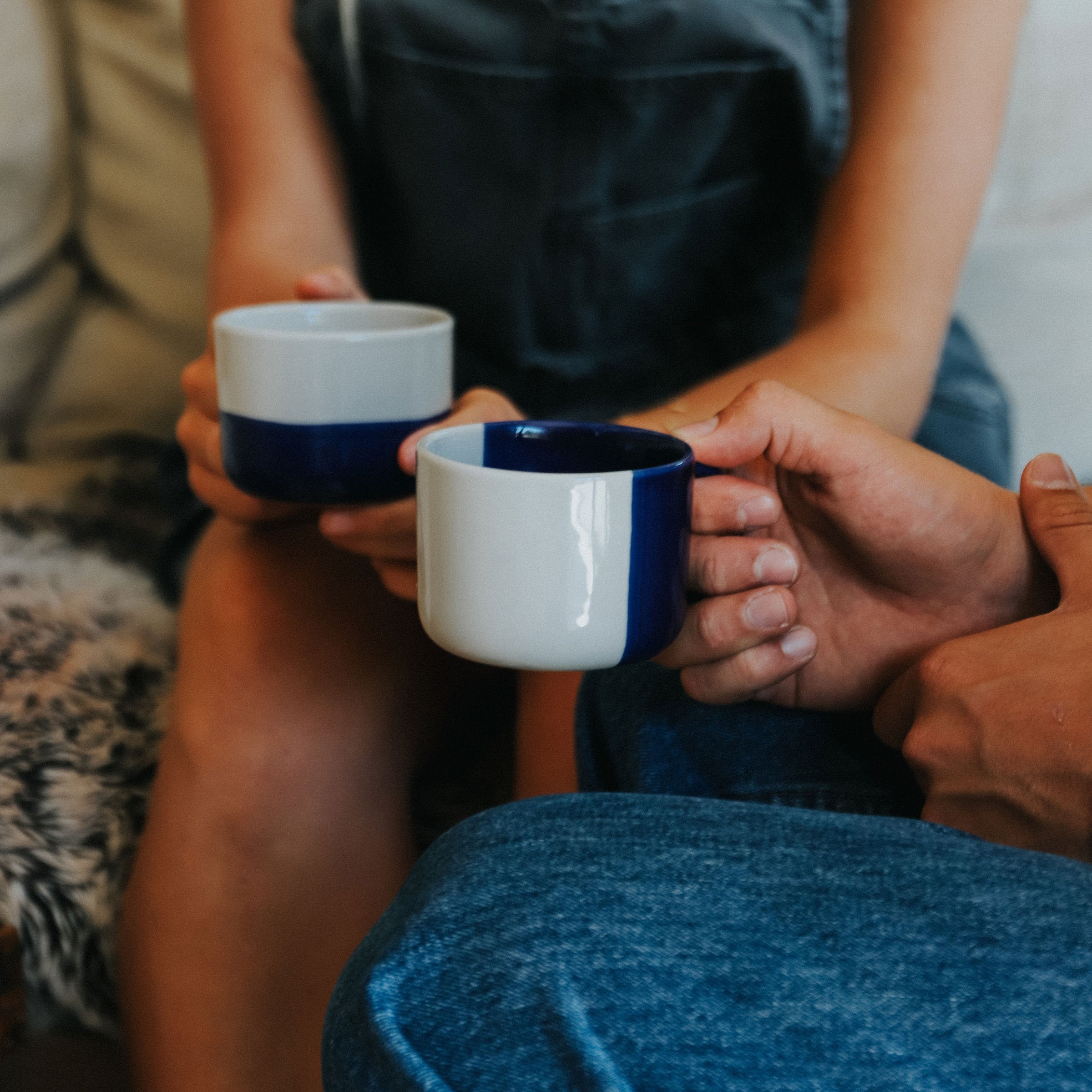 Two people holding indigo blue Rue mugs on a sofa