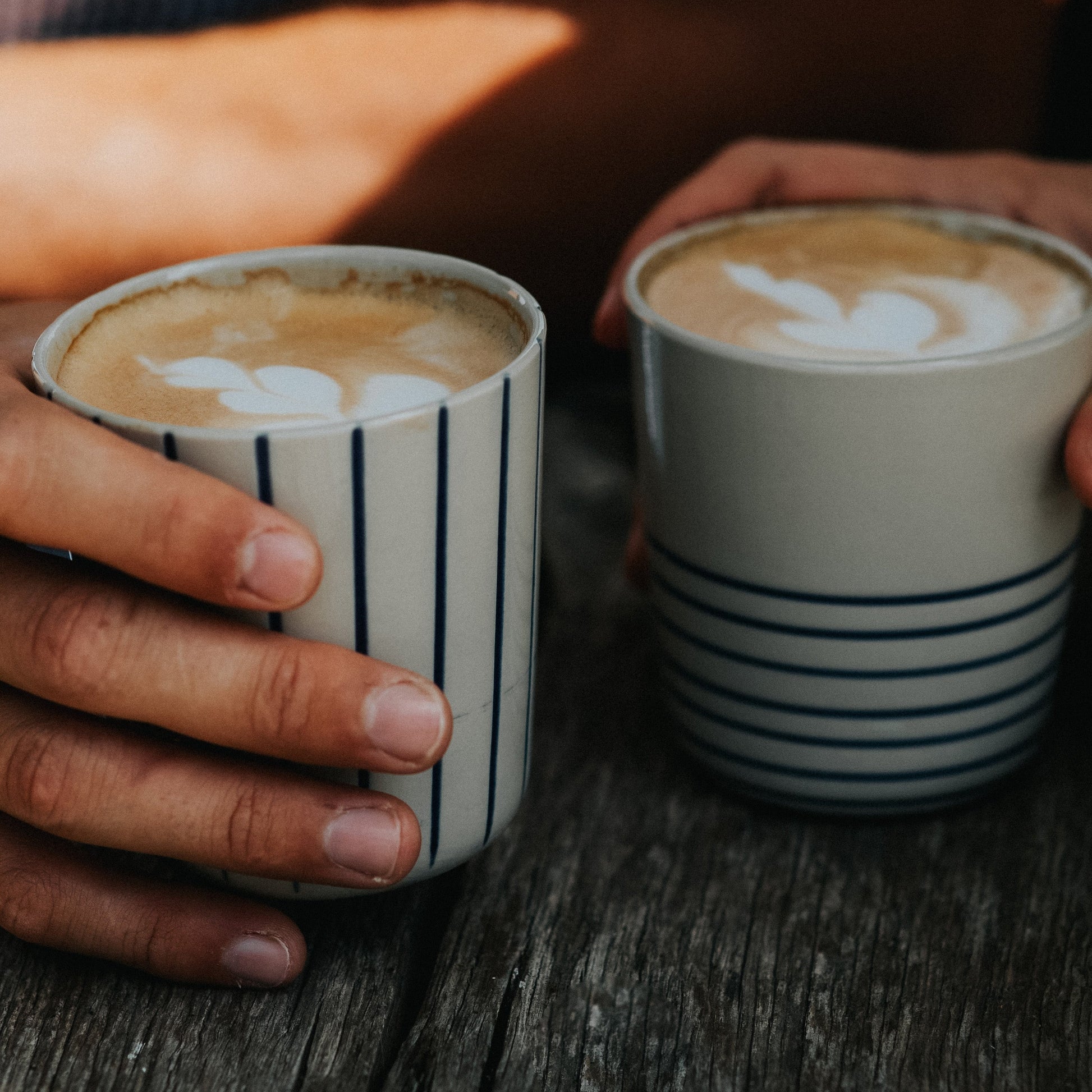 Hands holding two sea green Sorrel beakers filled with latte art