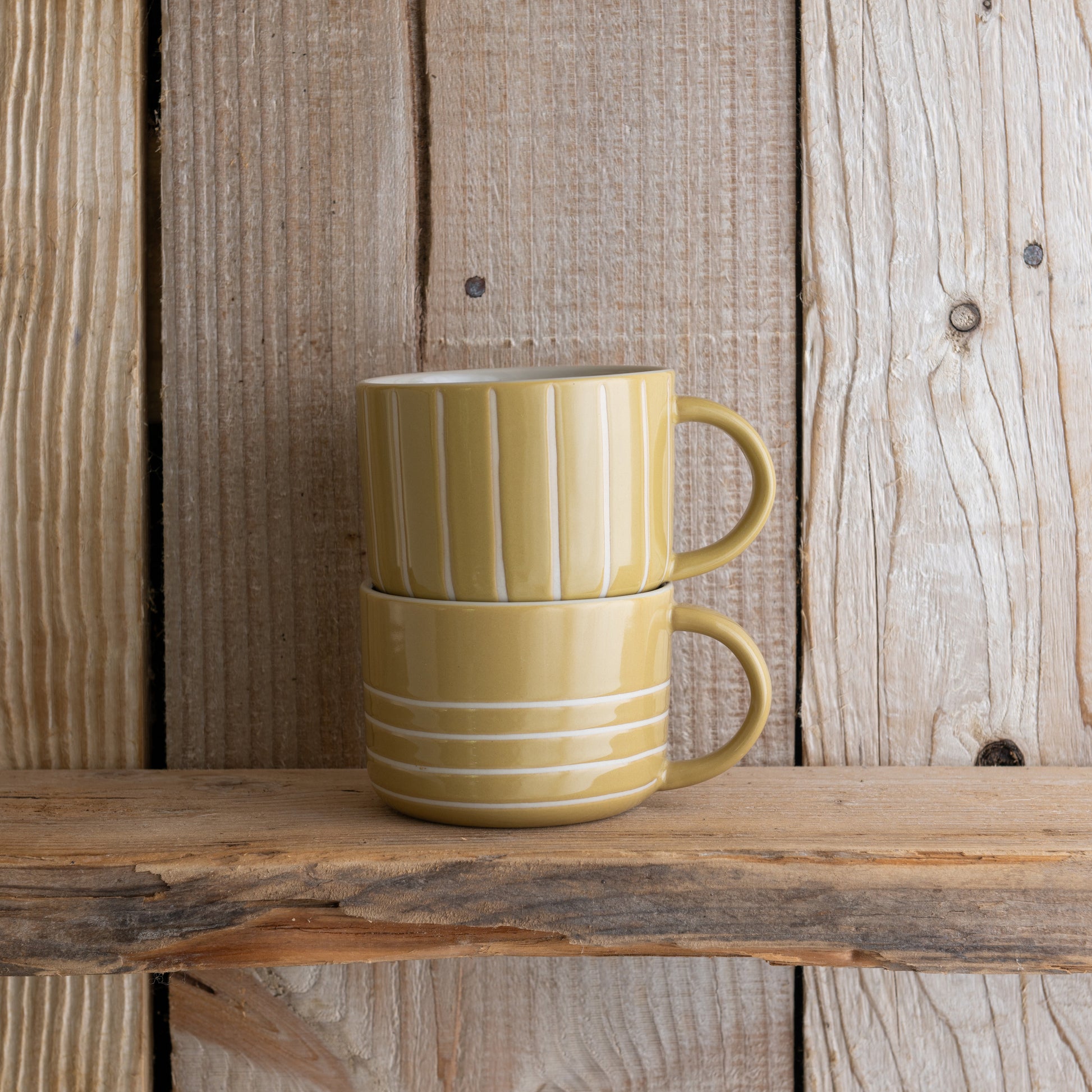 Mustard yellow Vervain mugs stacked on a weathered wooden shelf