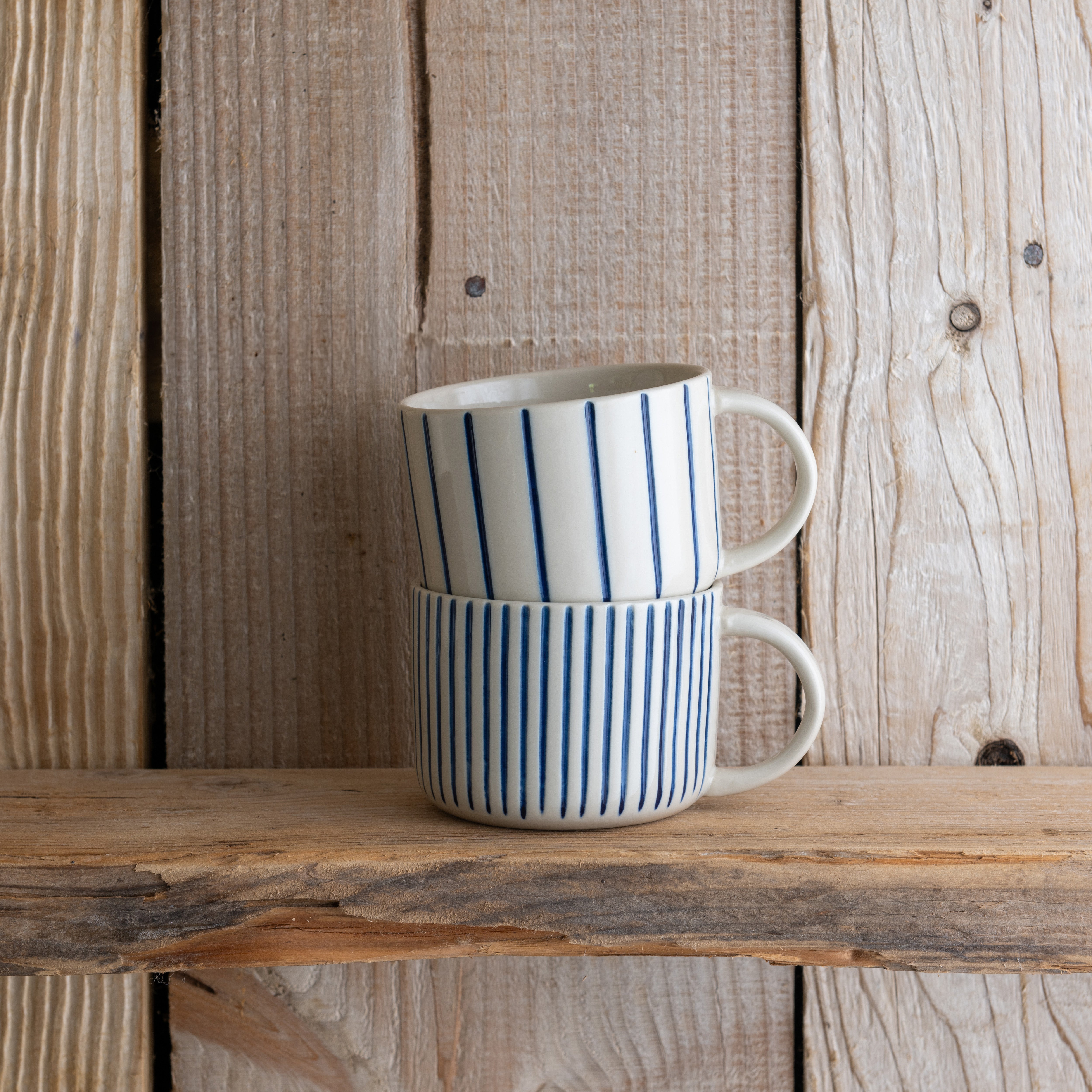 Indigo blue Yarrow mugs stacked on a weathered wooden shelf