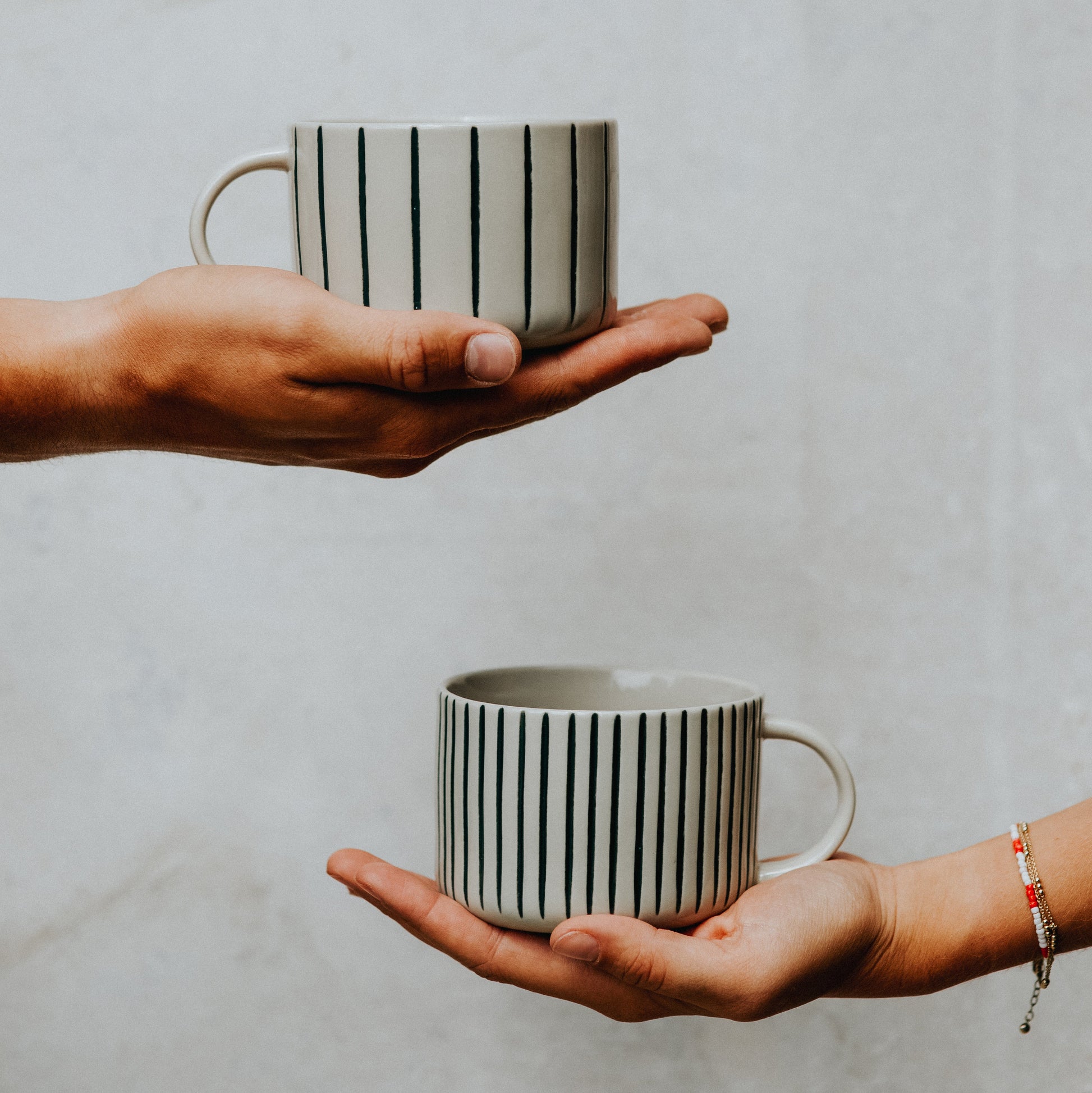 Two hands each holding a sea green Yarrow mug