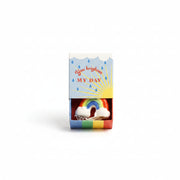 Ceramic rainbow inside open blue matchbox with sunshine and raindrop design on cream background