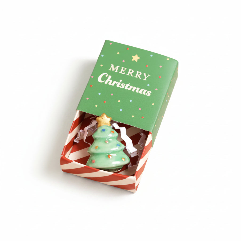 Ceramic Christmas tree token in an open Merry Christmas matchbox on cream