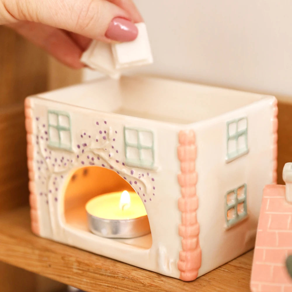 Cottage wax burner with a lit tealight glowing through the arched doorway