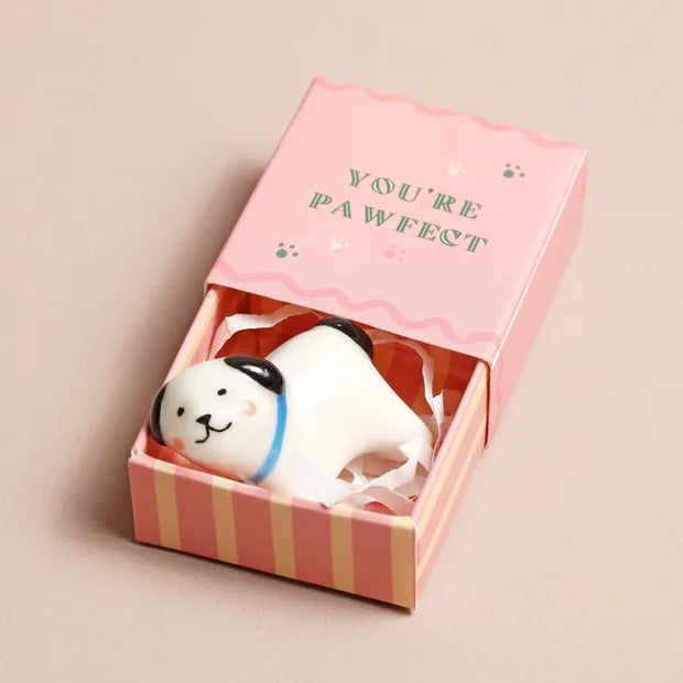 White ceramic dog token in open pink matchbox on beige surface