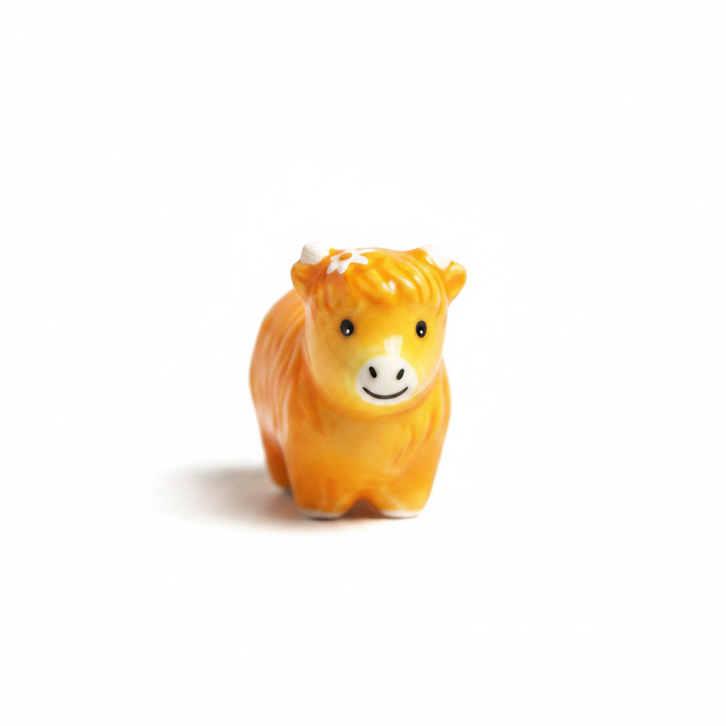 Ginger ceramic Highland cow token with a daisy, beside its matchbox