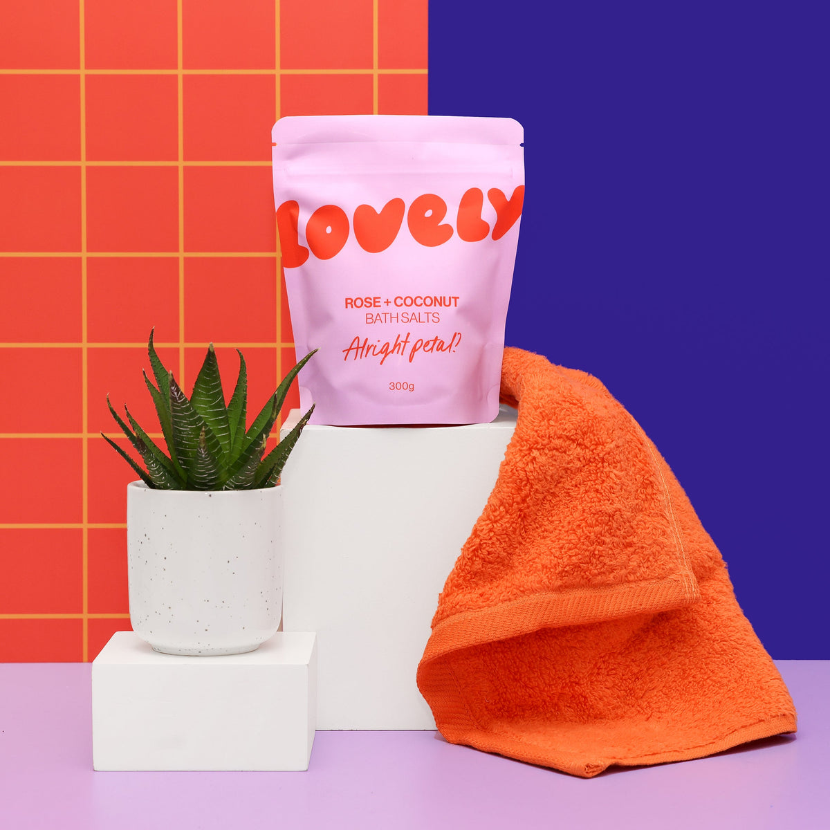 Rose and Coconut bath salts on a shelf with a plant and towel